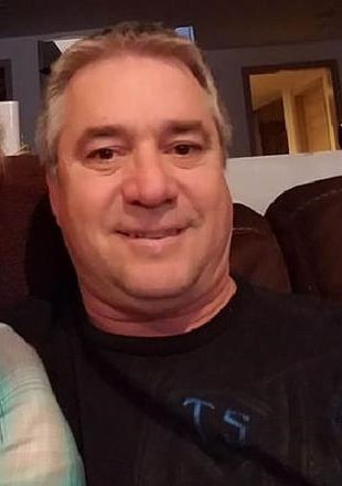 A man is sitting on a couch wearing a black shirt and smiling.