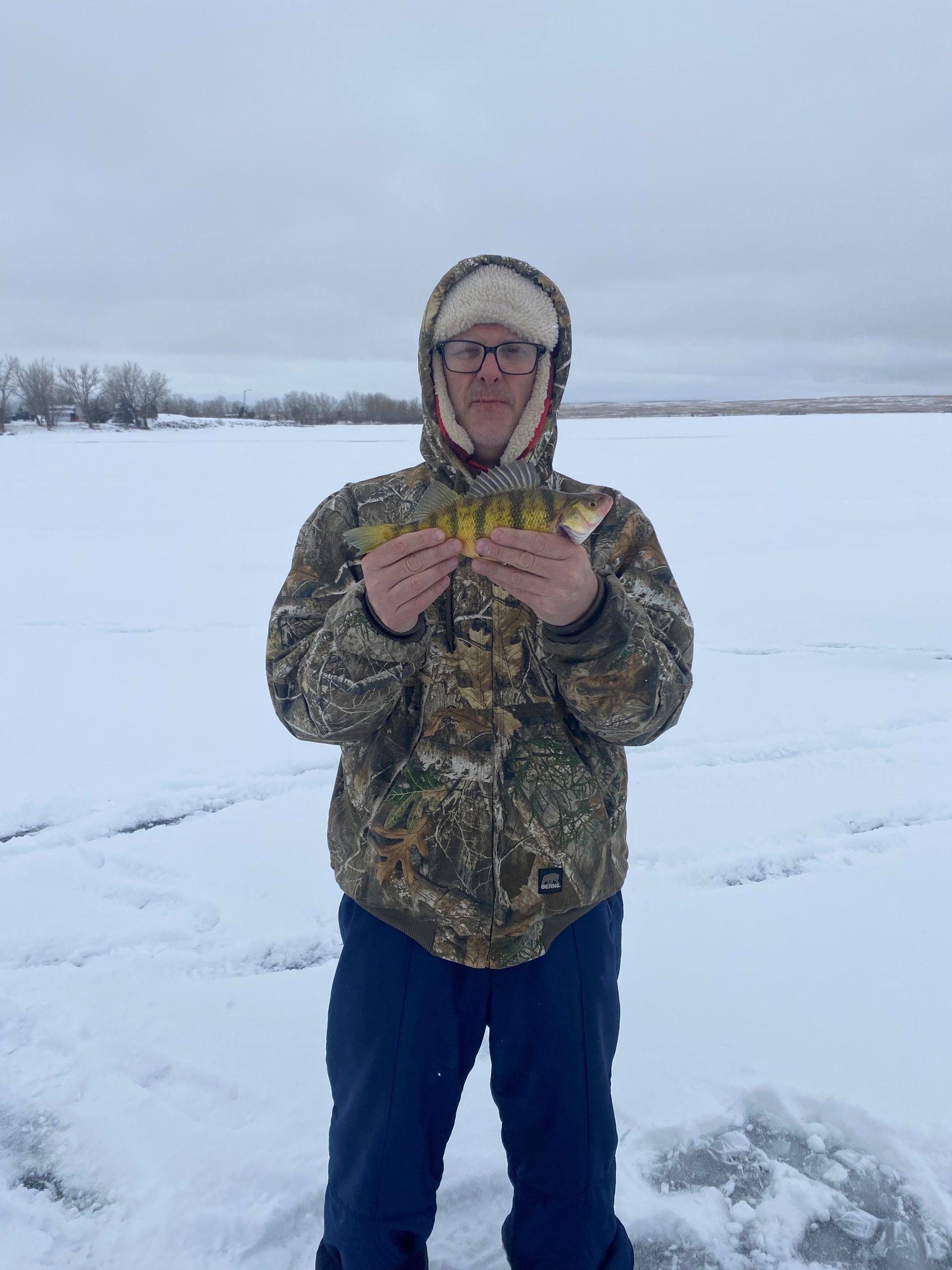 a man is standing in the snow holding a fish in his hands.