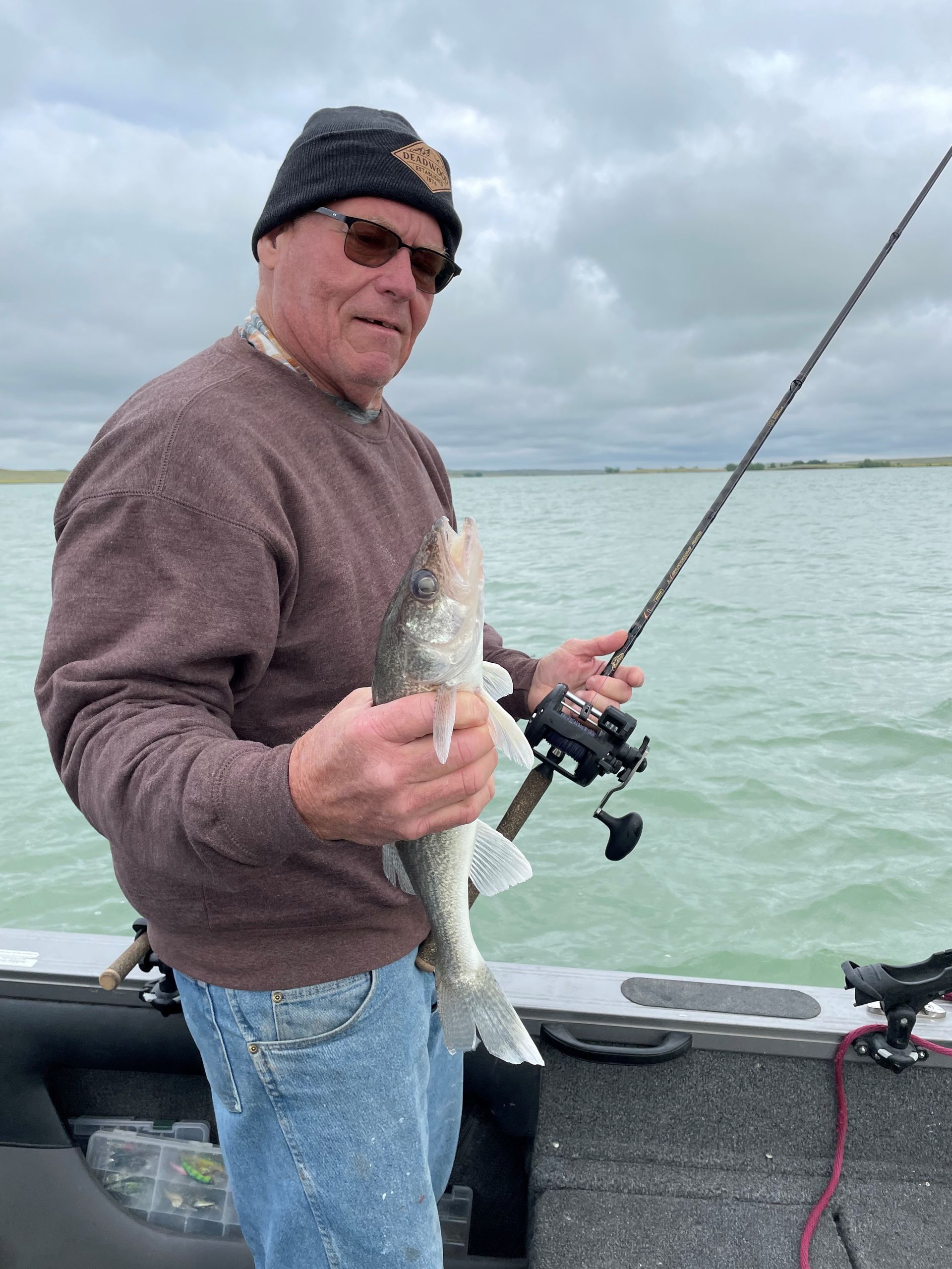 A man is holding a fish and a fishing rod on a boat