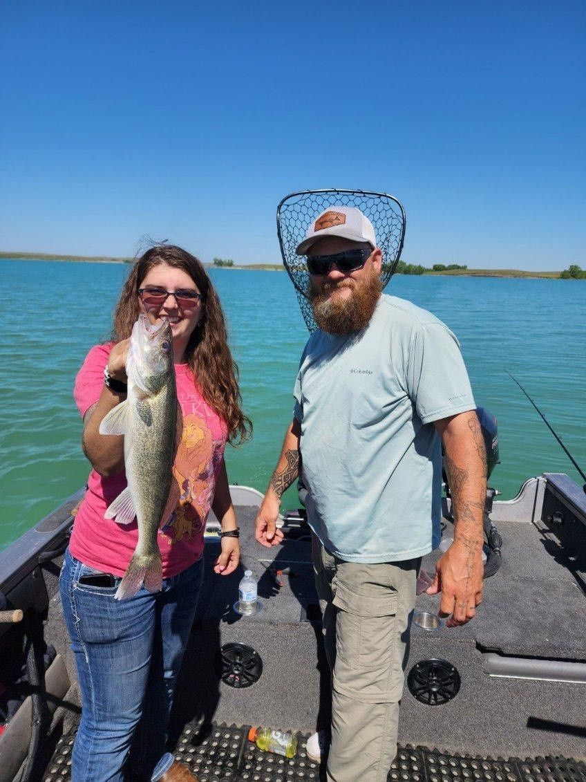 A man and a woman are standing on a boat holding a fish