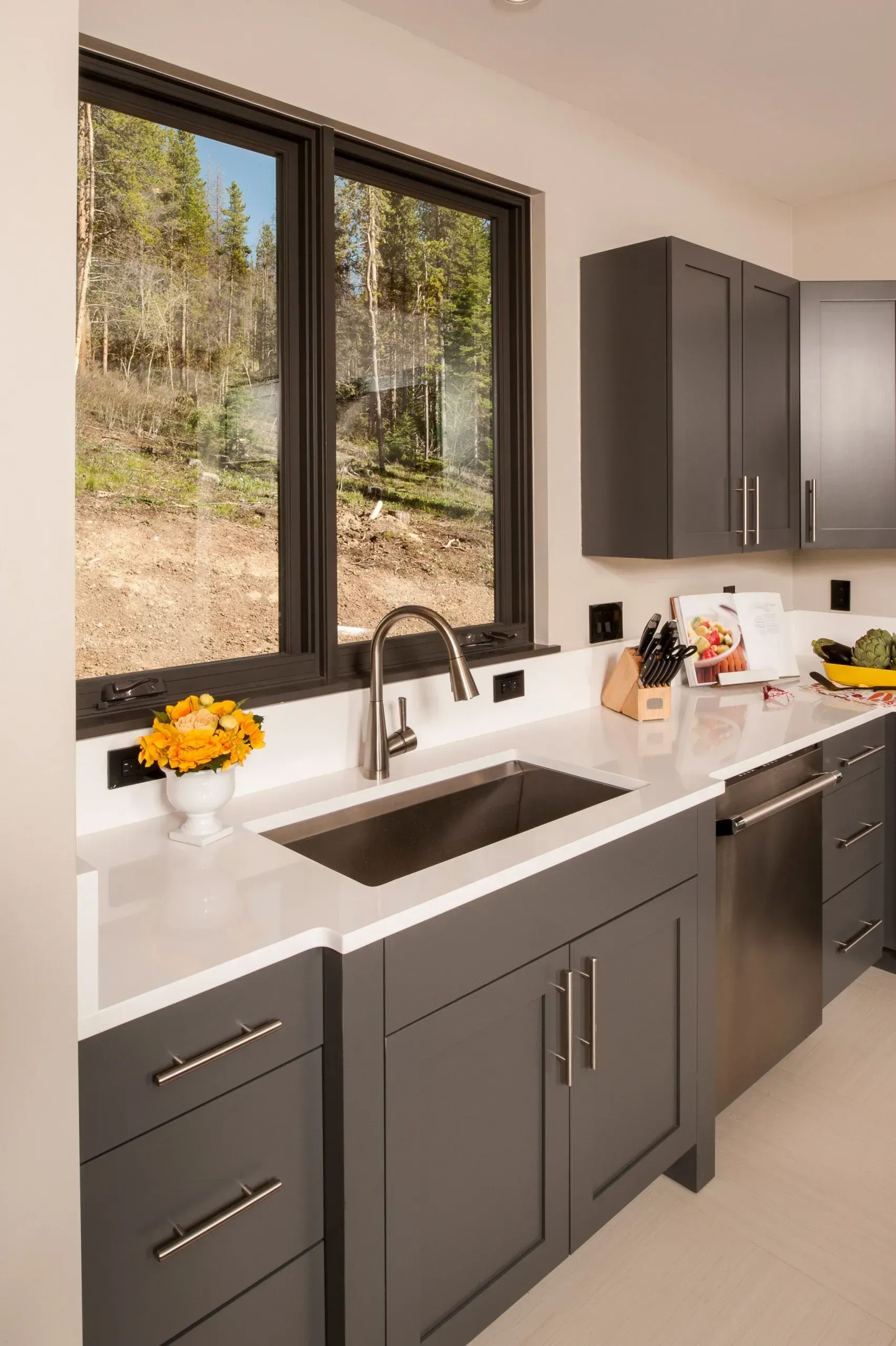 Gray kitchen with white countertops, stainless steel sink and appliances, and a window with a view of trees.