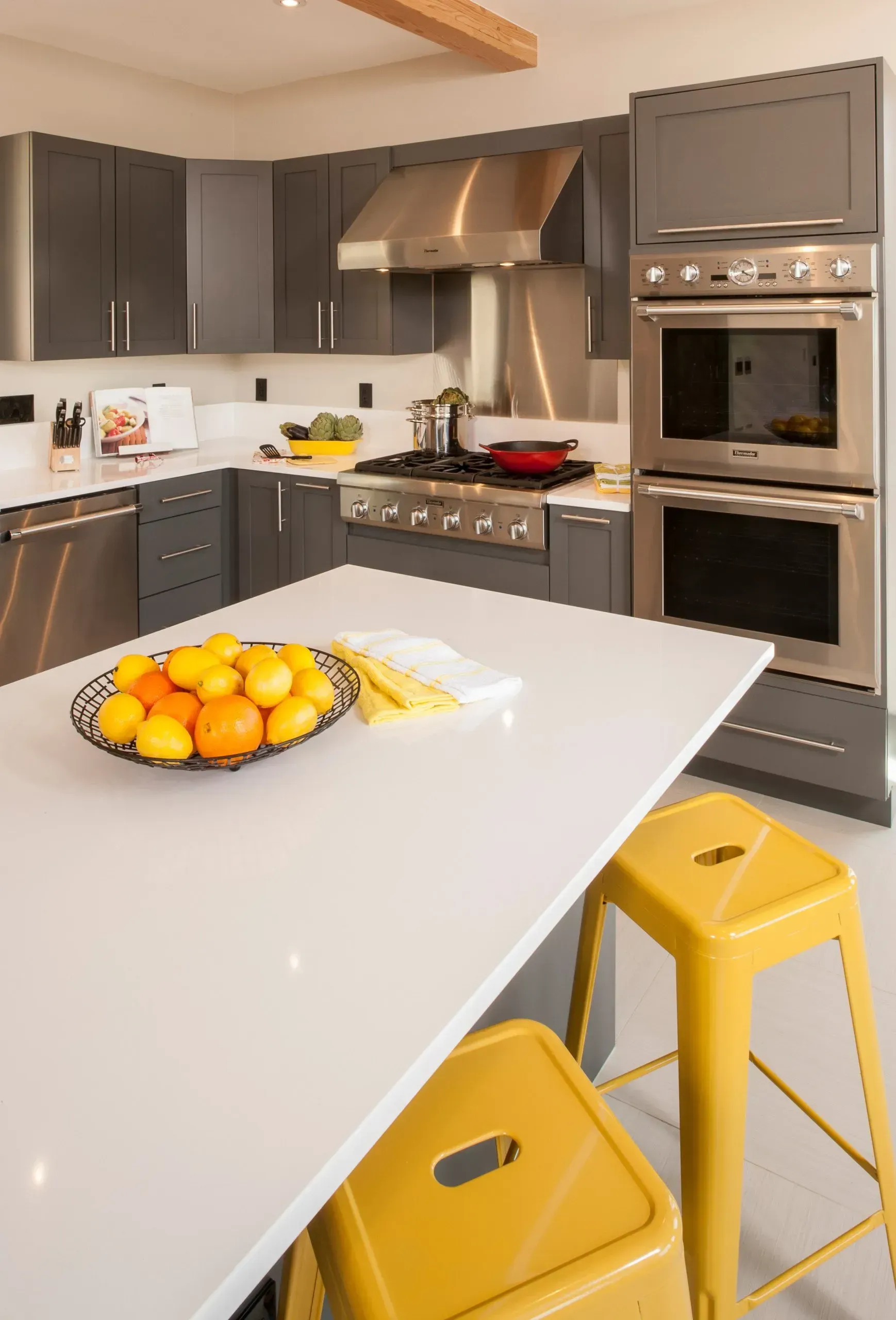 Modern kitchen with gray cabinets, stainless steel appliances, white countertop island, and yellow stools.