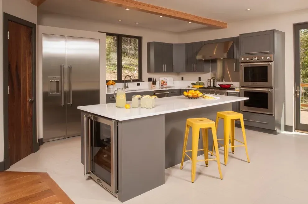 Modern kitchen with gray cabinets, white countertop island, yellow stools, and stainless steel appliances.