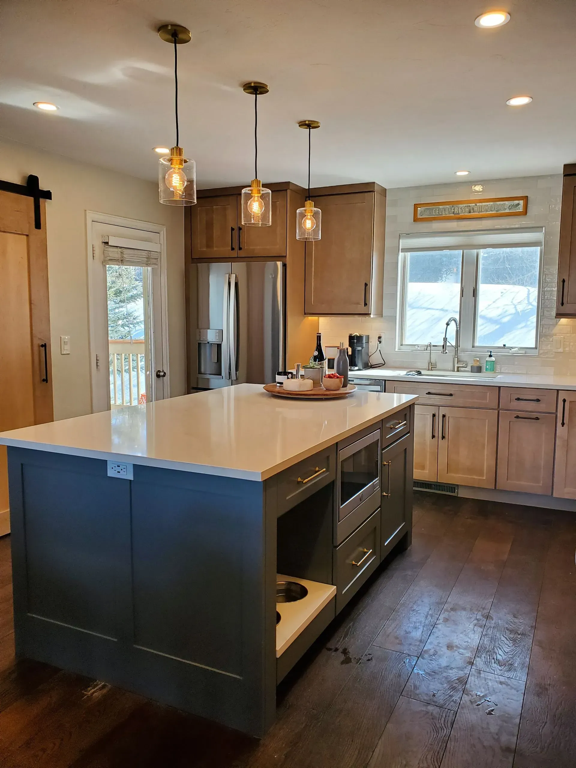 Kitchen with green island, light wood cabinets, three pendant lights, stainless steel appliances, and a dark wooden floor.