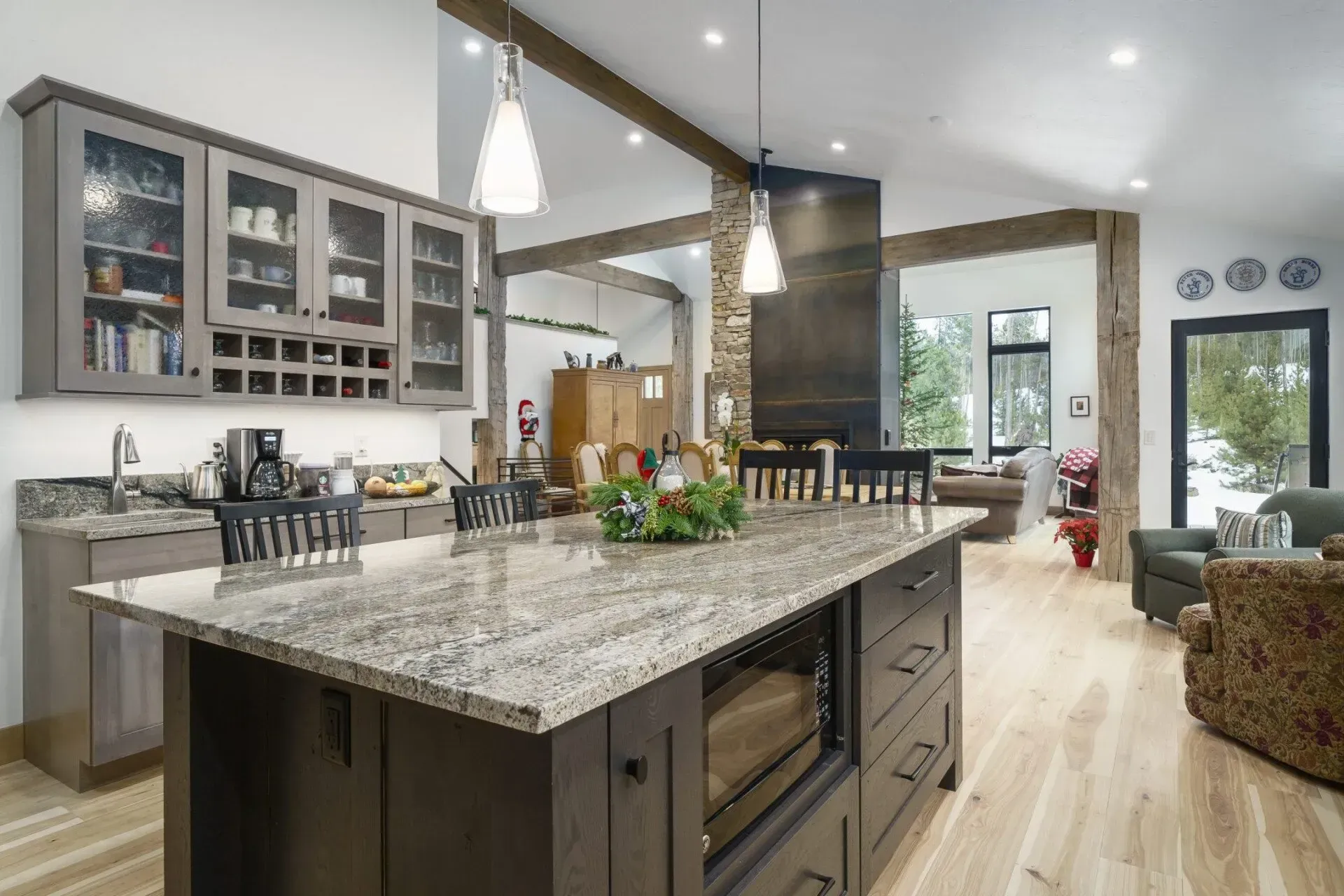 Open-concept kitchen with granite island, wood cabinets, and exposed beams; living room visible.