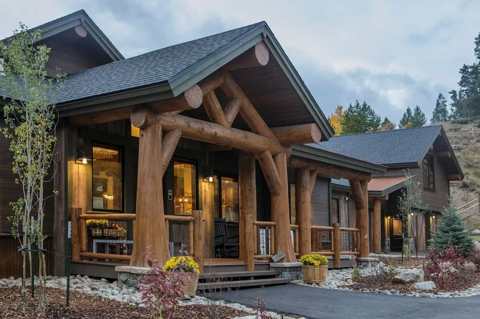 Wooden cabin with covered porch, rocky landscaping, and a dark roof.