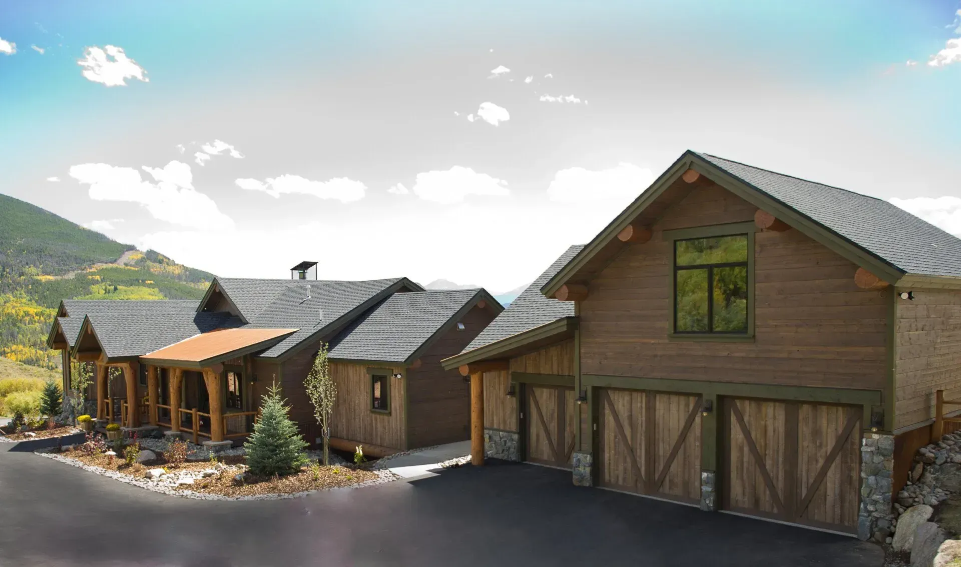 Mountain home with wood siding, stone accents, and a two-car garage under a partly cloudy sky.
