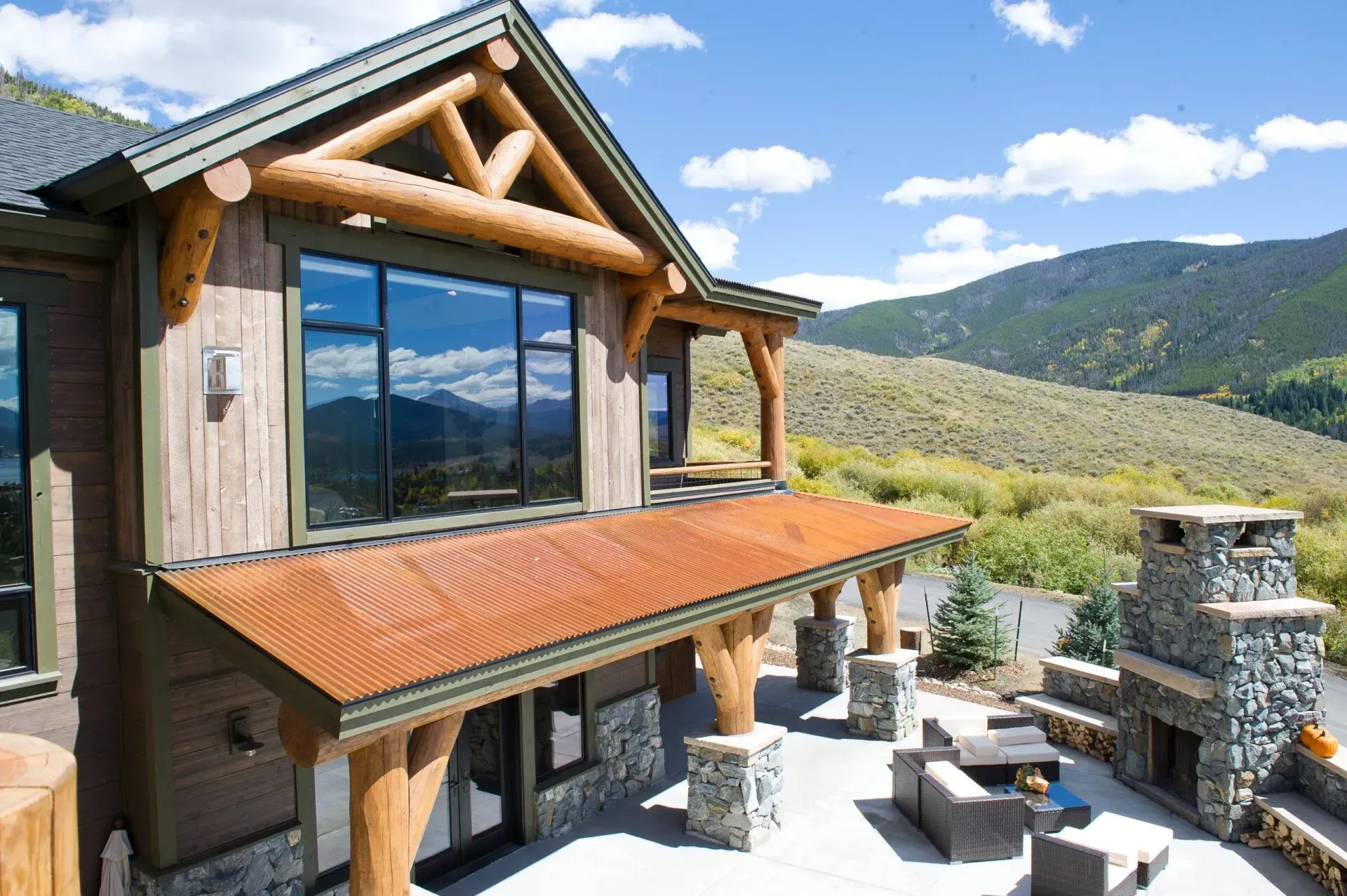 Rustic home with large windows, covered patio, stone fireplace, and mountain view.