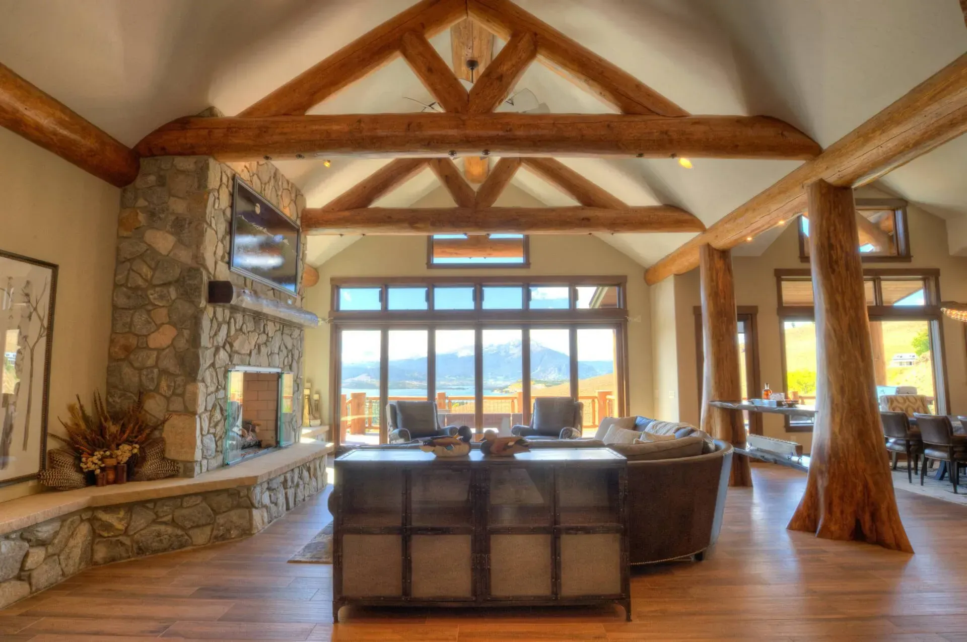 Living room with stone fireplace, wooden beams, large windows, and leather furniture.