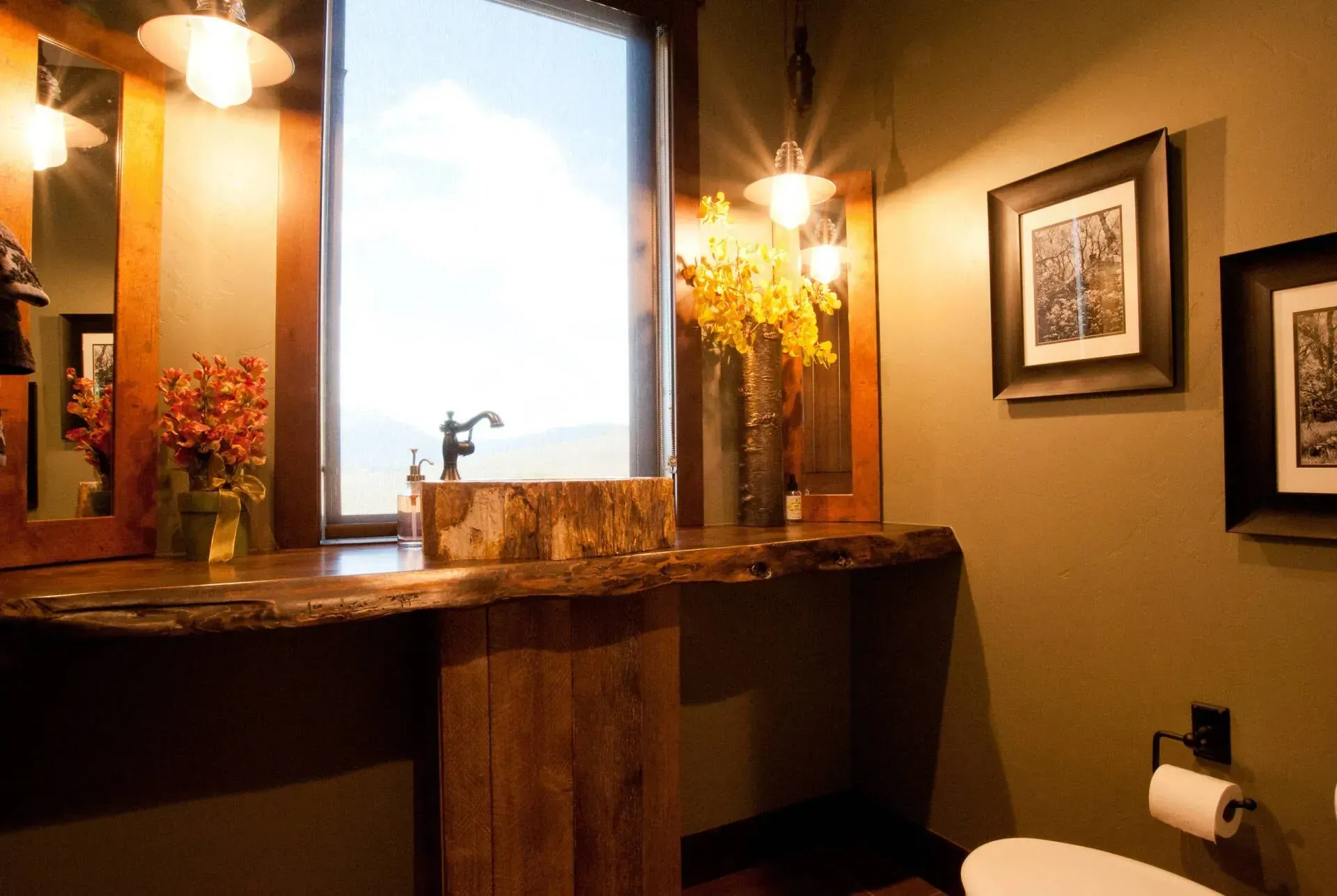 Rustic bathroom with wood vanity, large window overlooking mountains, and framed art.