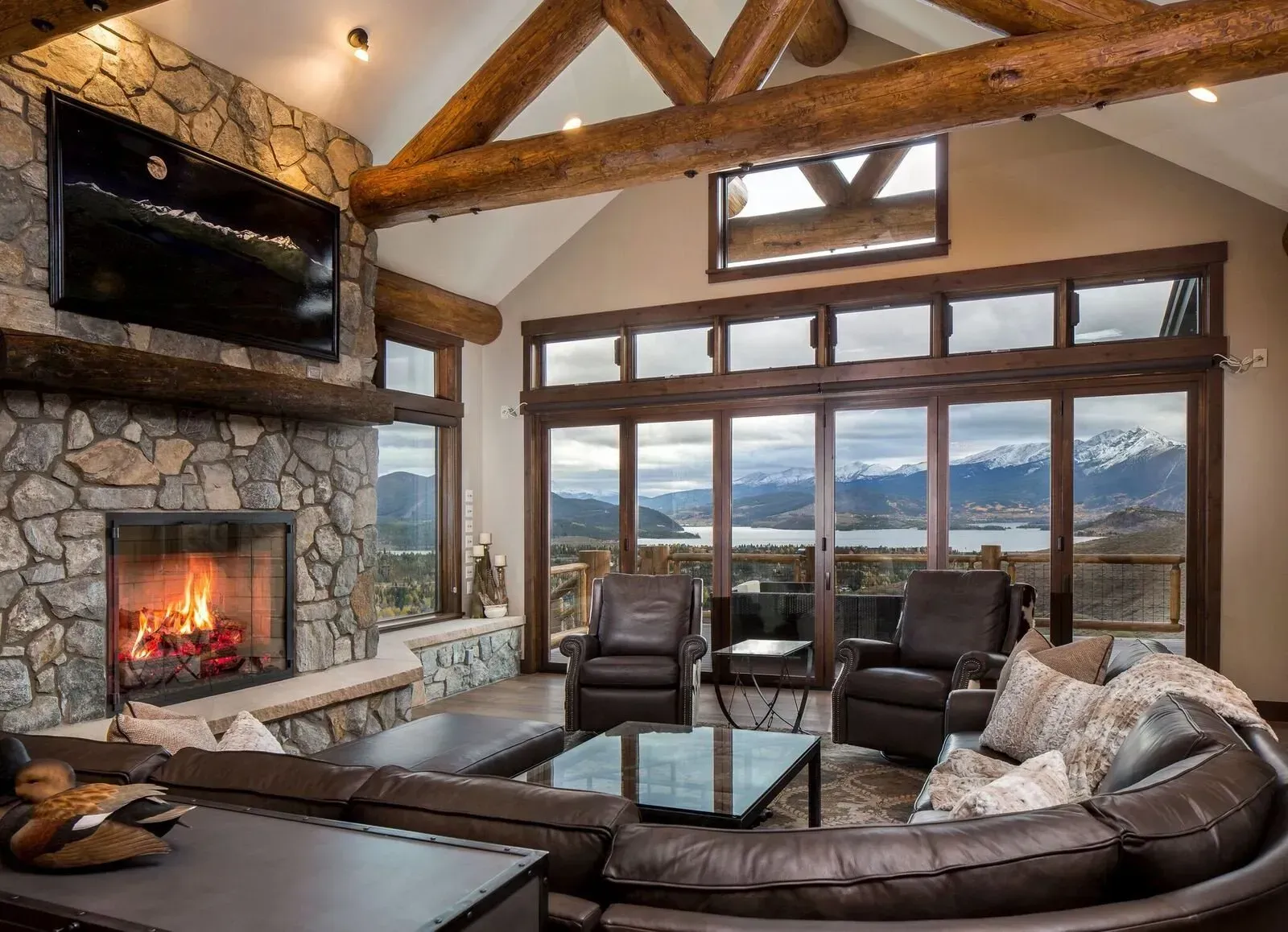 Cozy living room with stone fireplace, large windows, leather furniture, and mountain views.