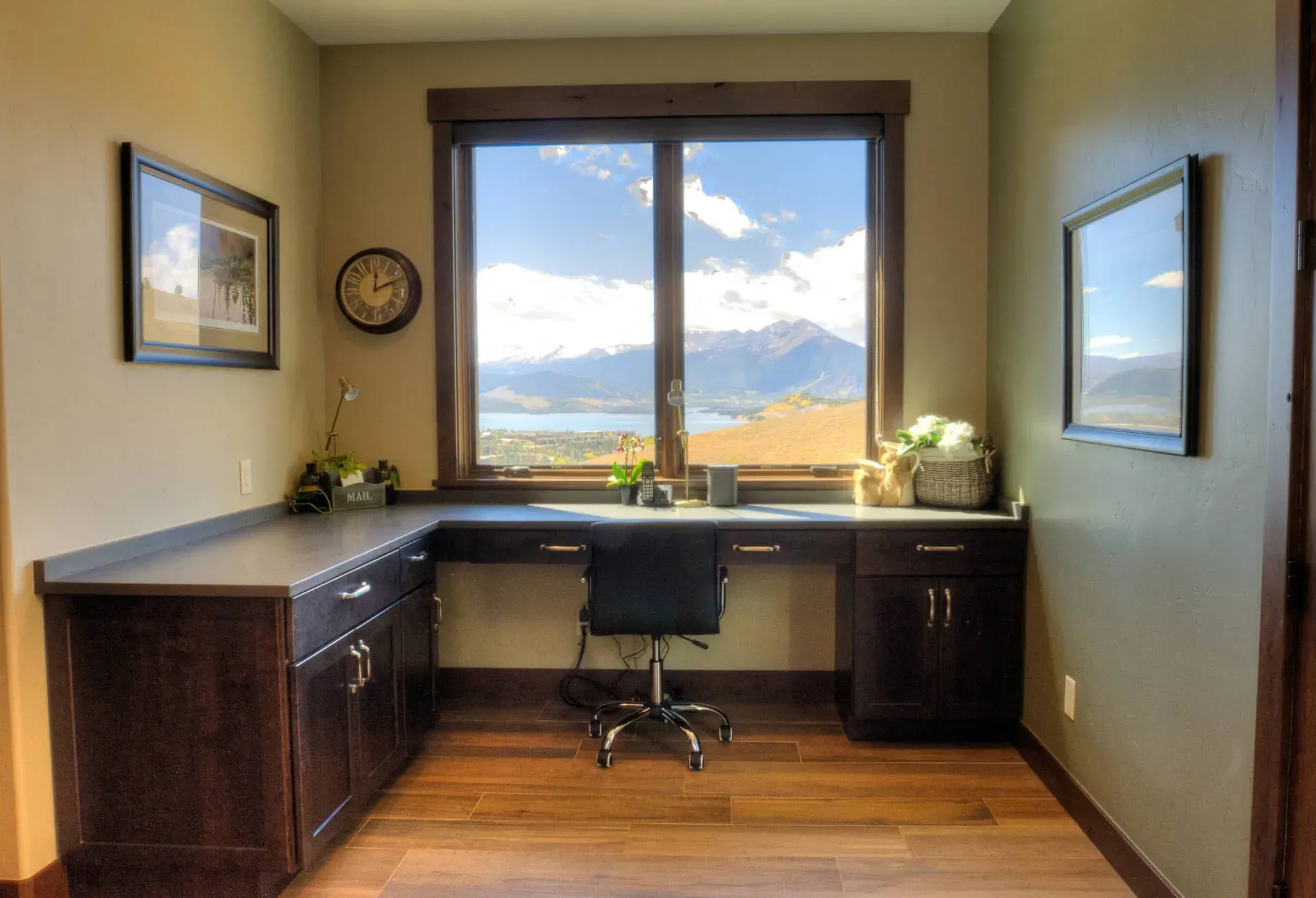 Home office with a dark wood desk, cabinets, and a large window framing a scenic mountain view.