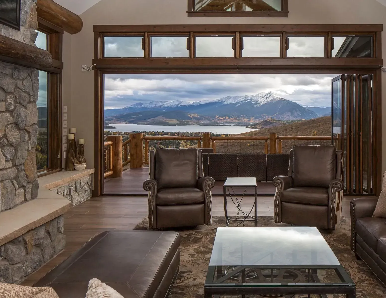 Living room with brown leather furniture, large folding doors, mountain and lake view.
