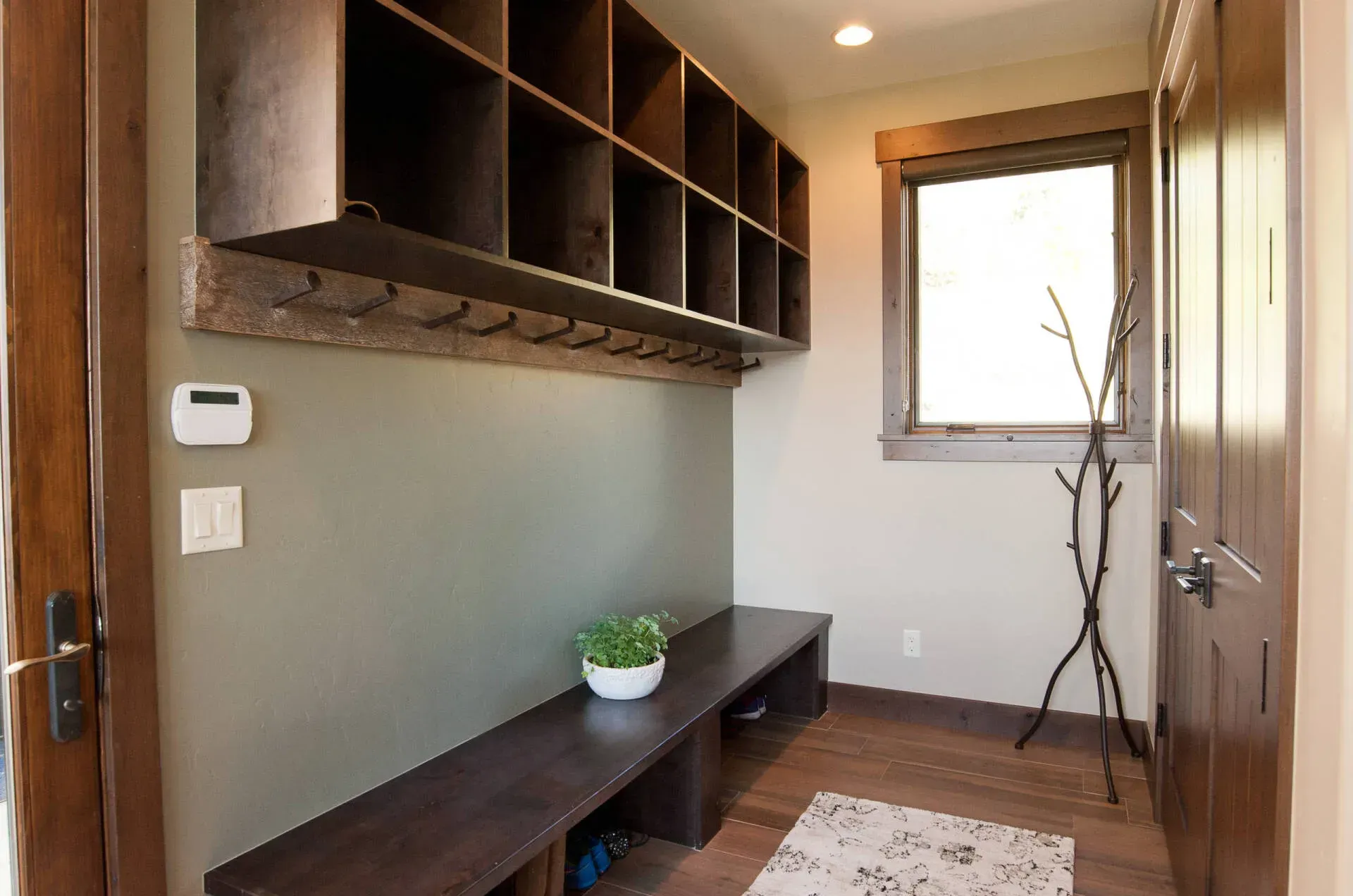 Mudroom with wooden bench, cubbies, and coat hooks; sage green wall and wooden door.