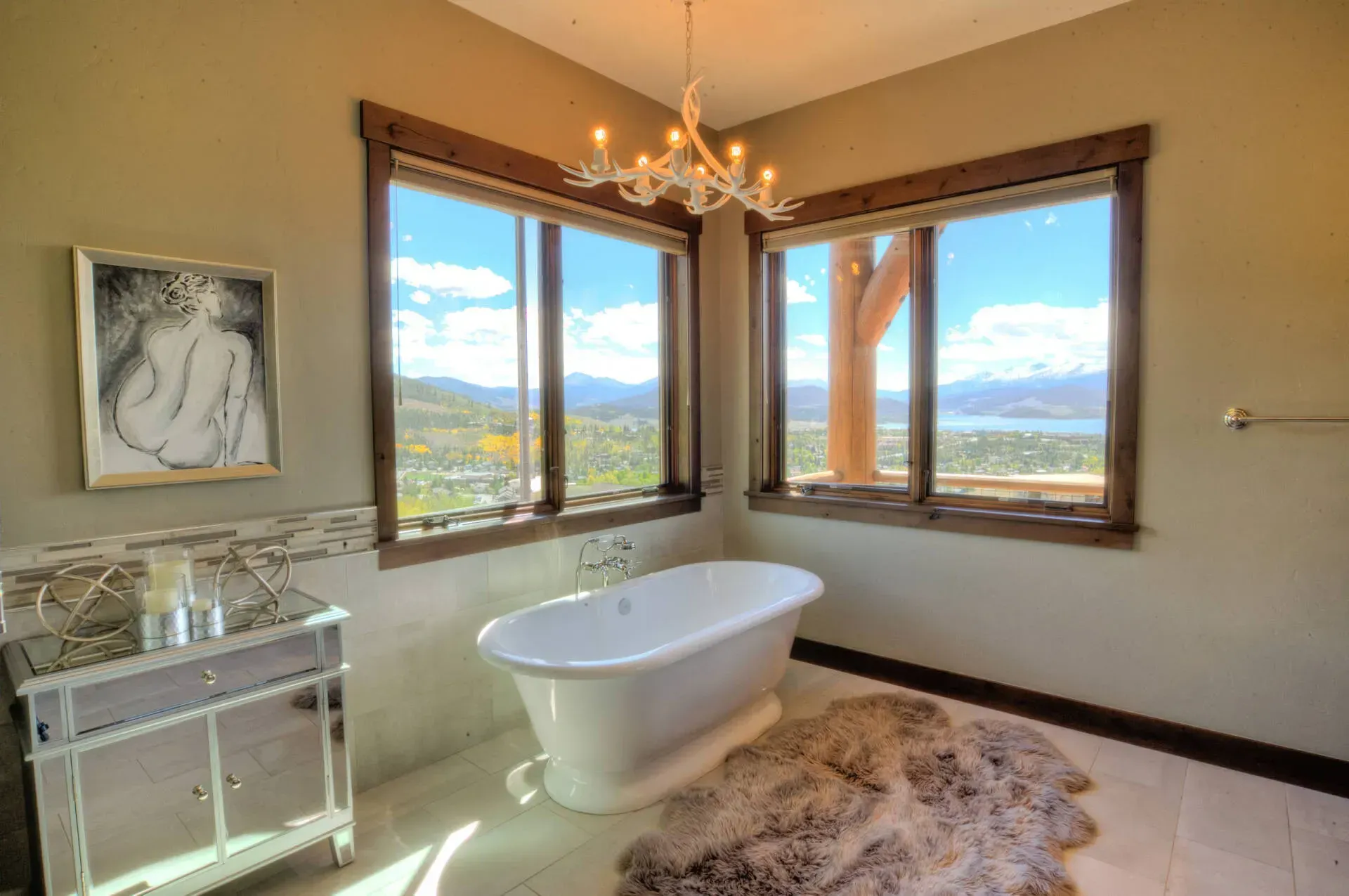 Bathroom with a white clawfoot tub, two large windows with a view, chandelier, and a decorative rug.