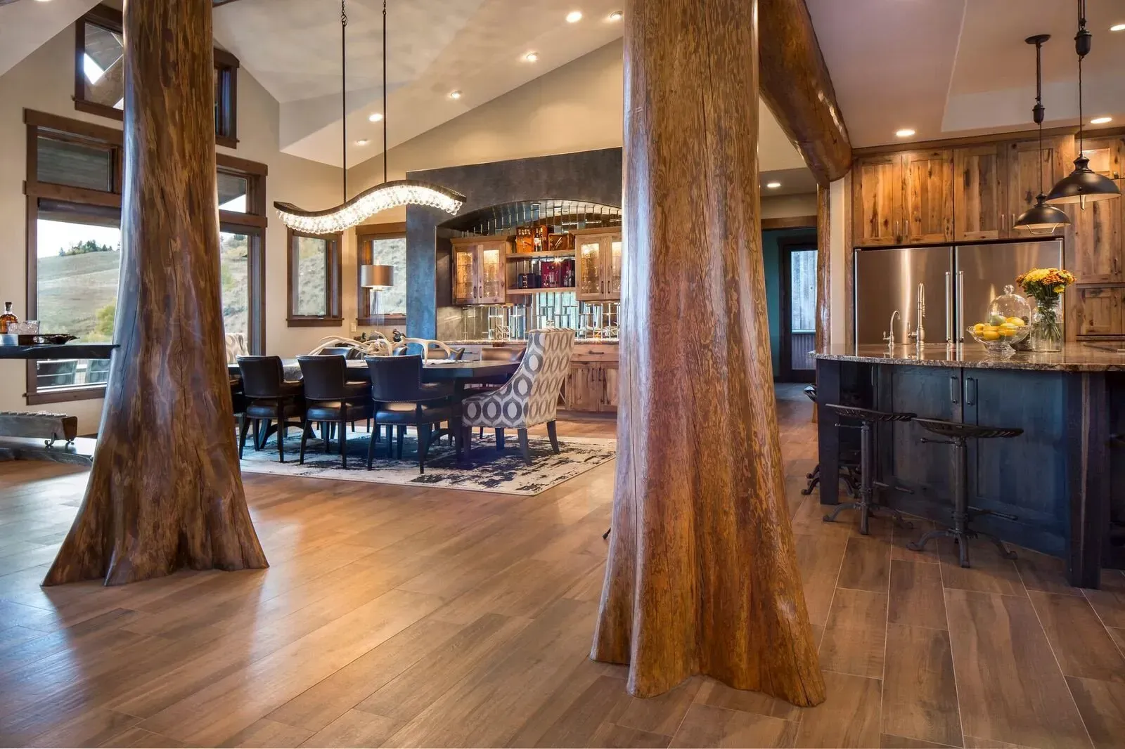 Rustic kitchen and dining area with hardwood floors, large tree trunk columns, and exposed wood accents.