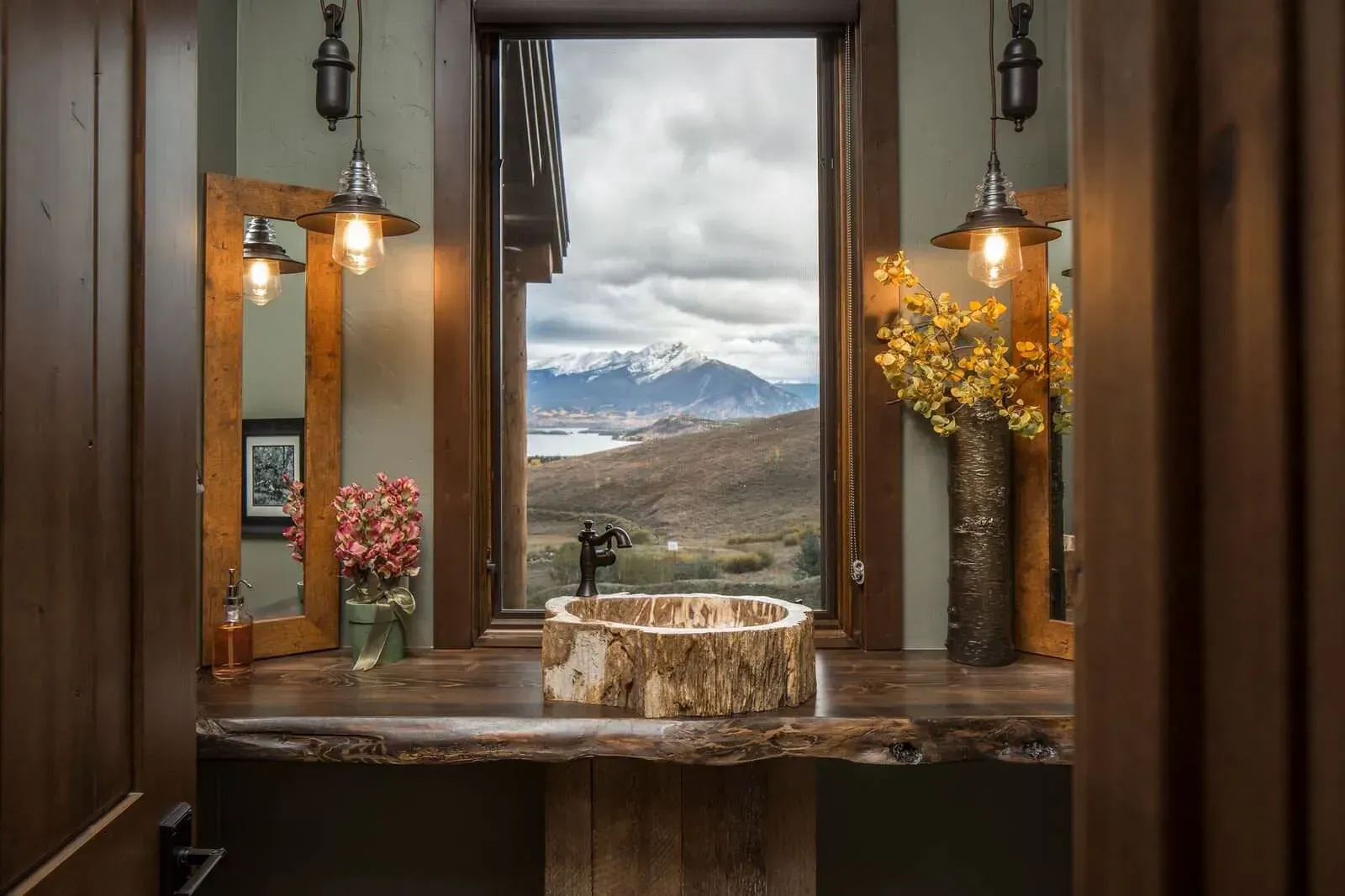 Bathroom with rustic wood countertop, large window with mountain view, and hanging lights.