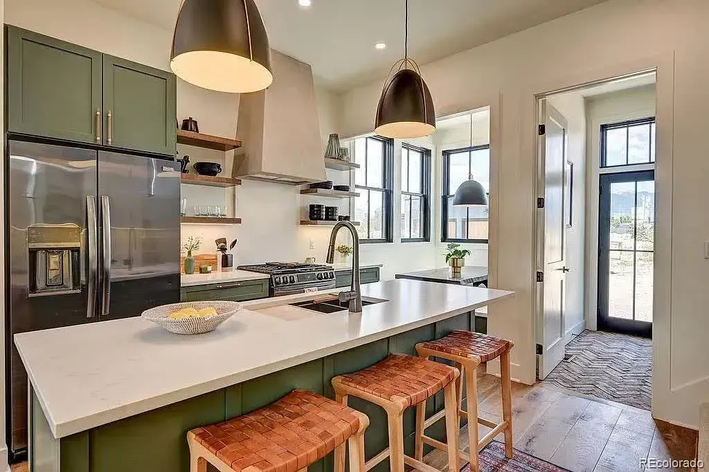 Modern kitchen with olive green cabinets, white countertops, and wooden stools.