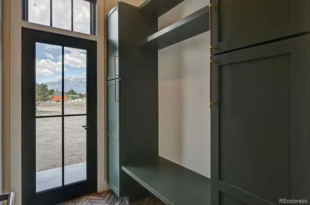 Dark green built-in cabinets with a desk and shelving, next to a black door with a view of a cloudy sky and mountains.