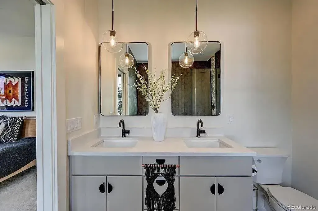 Bathroom with gray double vanity, black fixtures, two mirrors, and overhead globe lights.