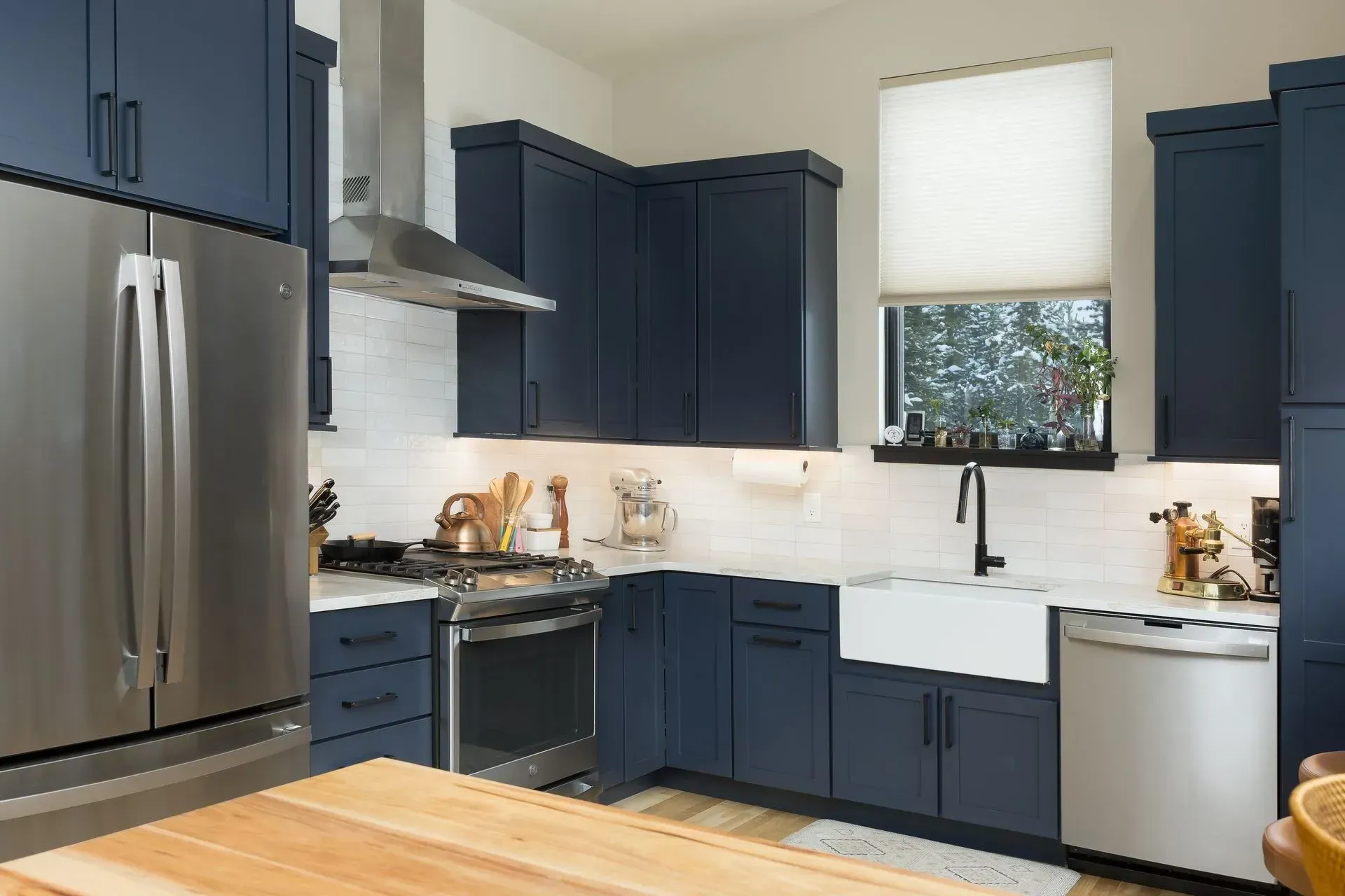 Blue kitchen with stainless steel appliances, white backsplash, and a farmhouse sink.