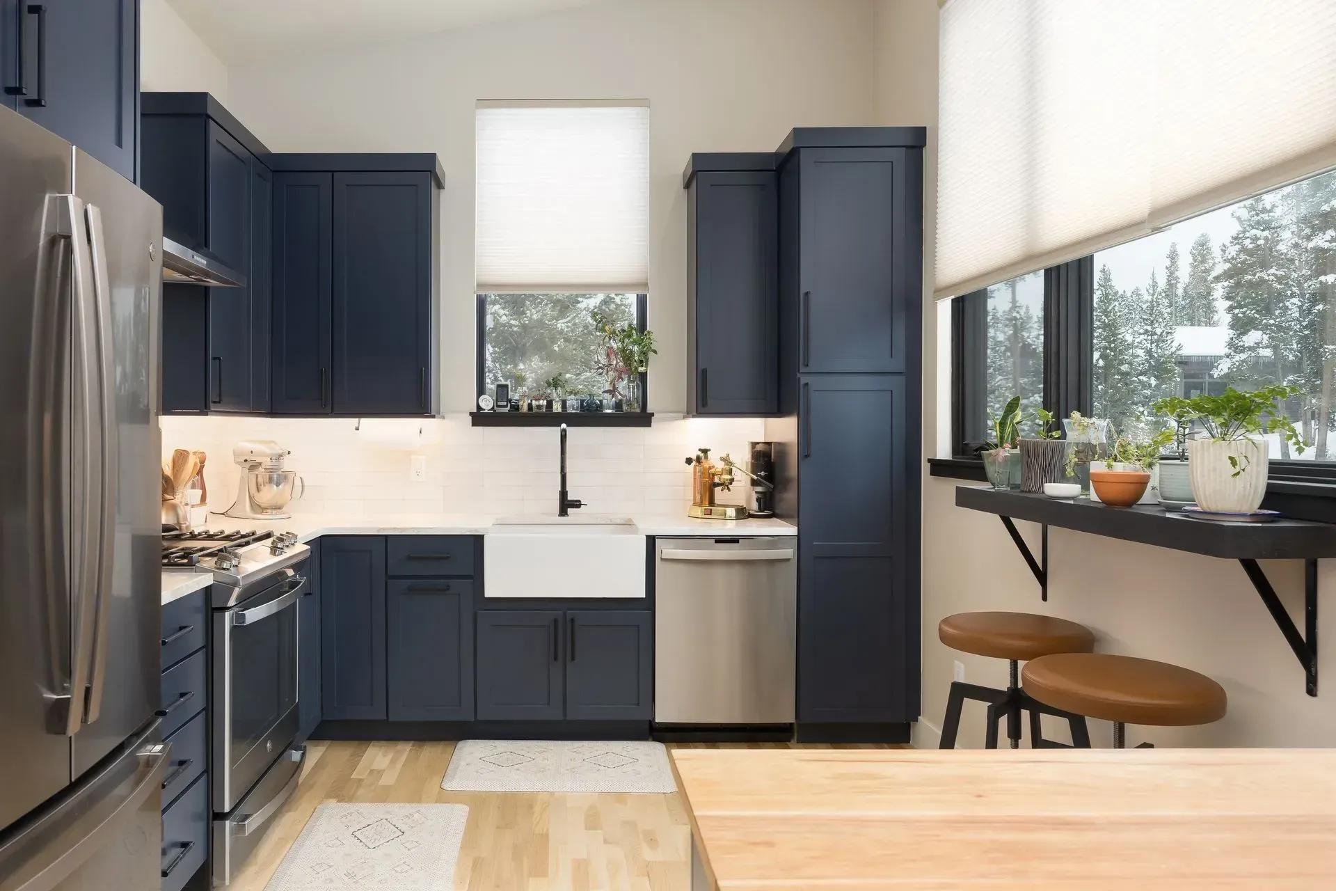 Navy blue kitchen with stainless steel appliances, white backsplash, and a window with plants.