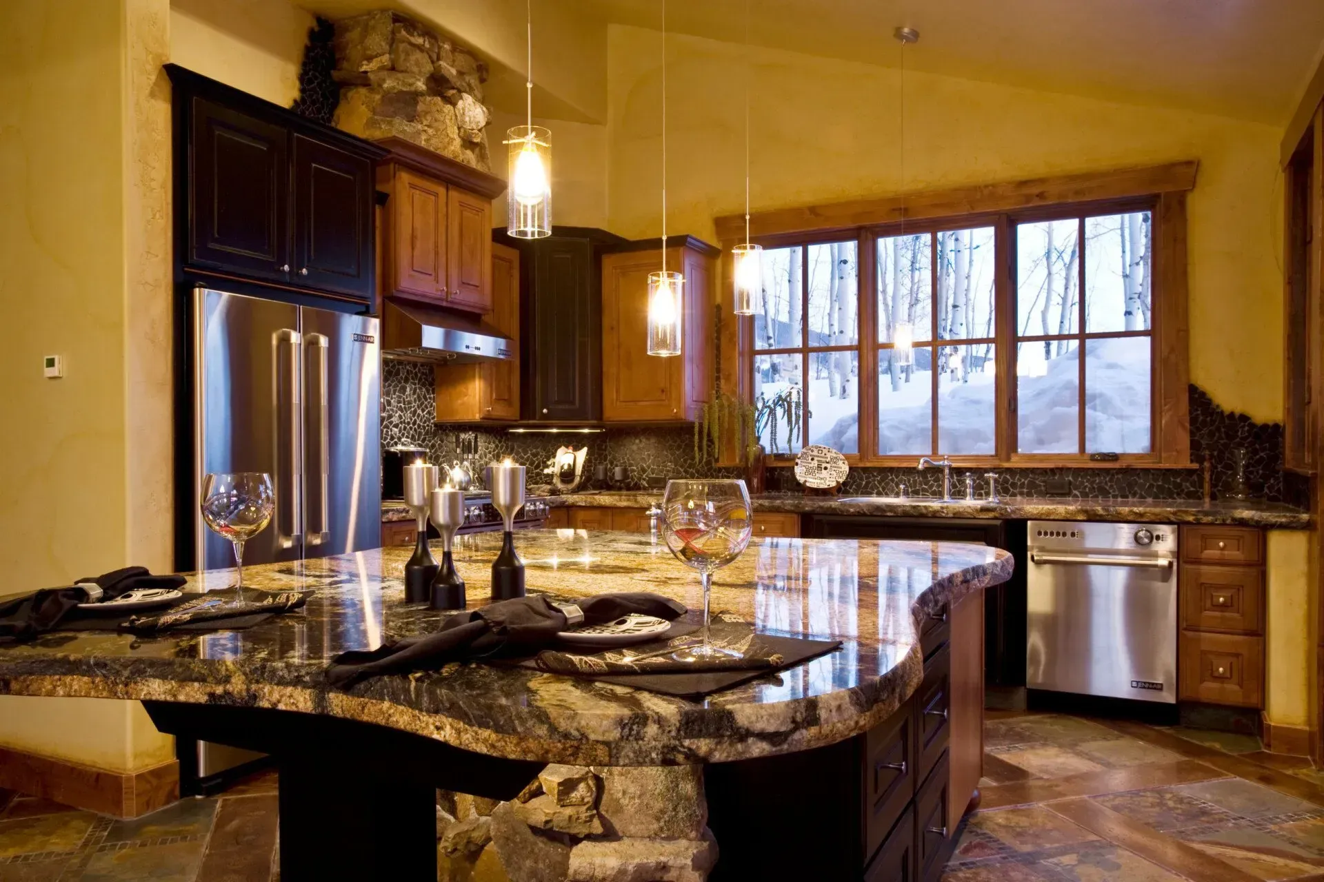 Kitchen with granite island, stainless steel appliances, and large window overlooking snowy trees.