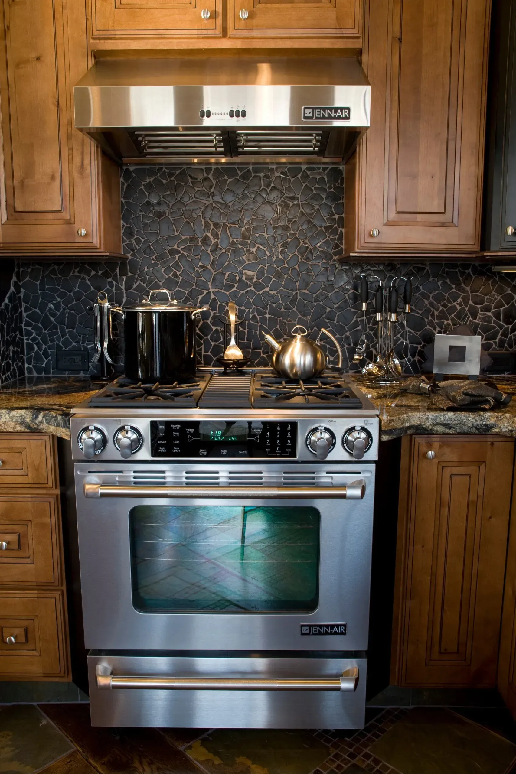 Stainless steel oven with range hood and wood cabinetry in a kitchen.