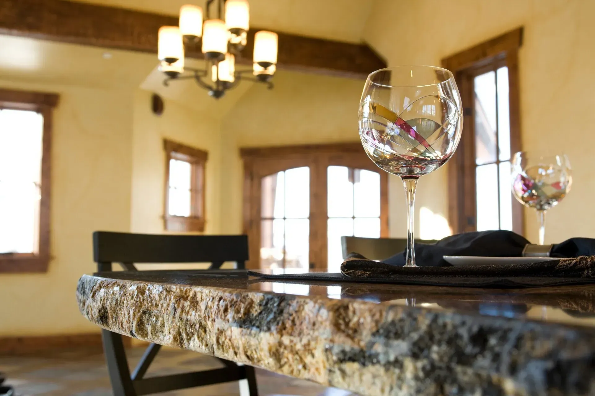 Close-up of a kitchen countertop with a wine glass, set with a blurry dining room in the background.