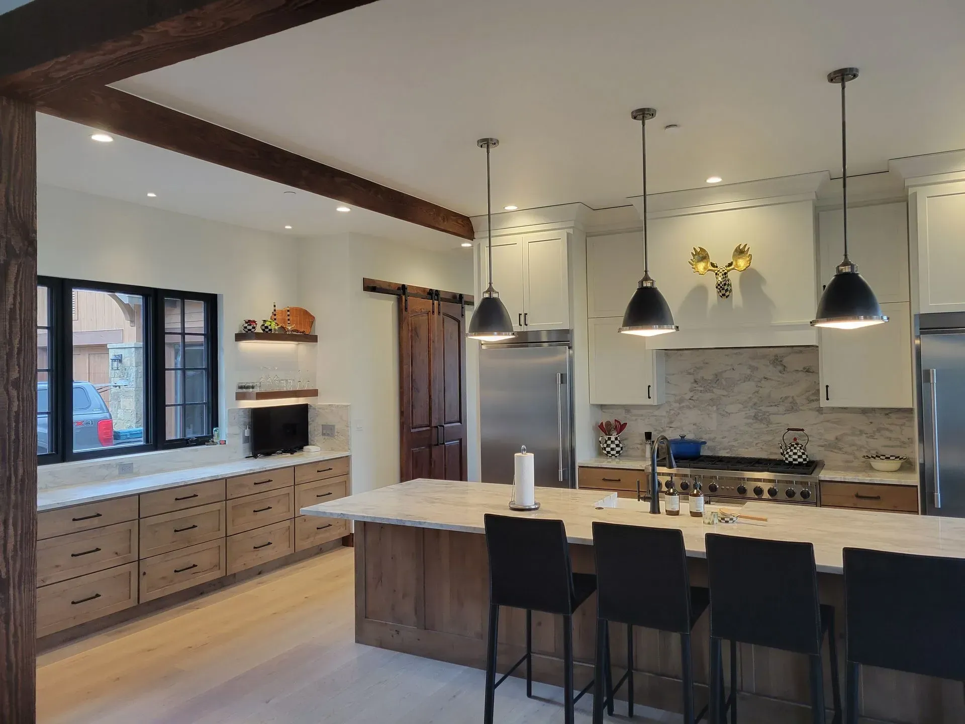 Modern kitchen with light wood cabinets, stainless steel appliances, and black pendant lights.