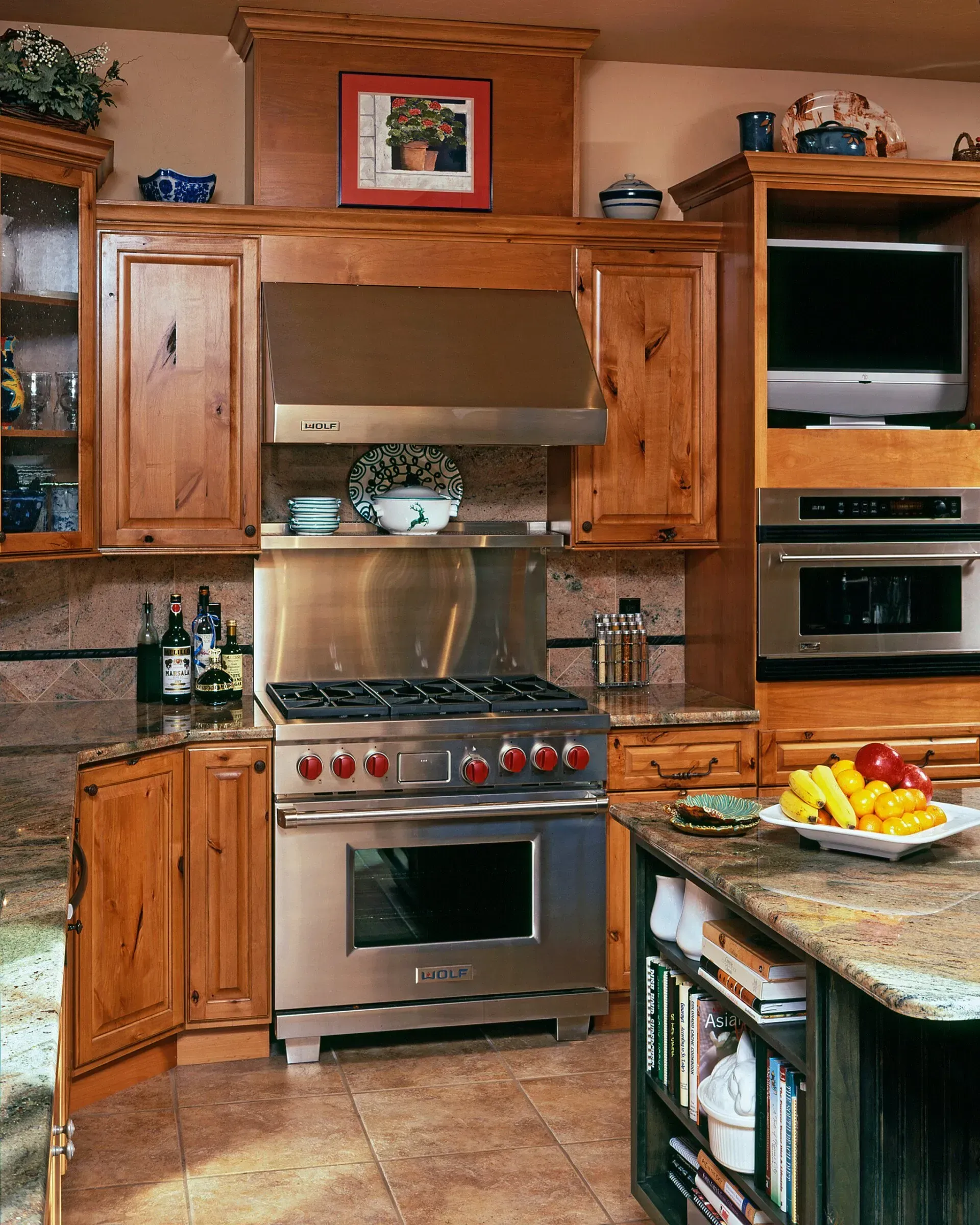 Kitchen with stainless steel range, wooden cabinets, built-in microwave, and TV. Island with fruit.