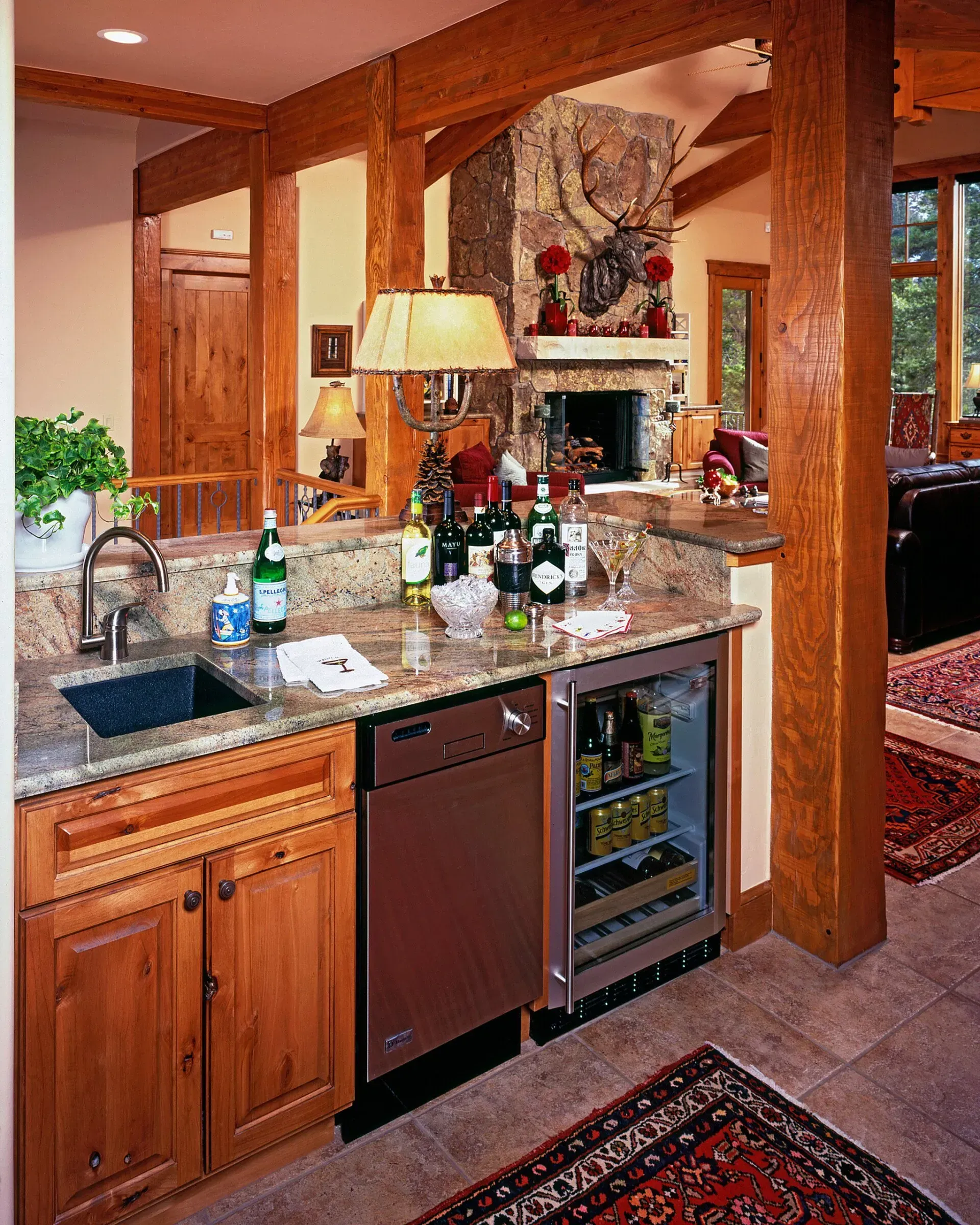 Rustic wet bar with granite countertop, sink, dishwasher, and mini-fridge; wooden beams and cabinets.