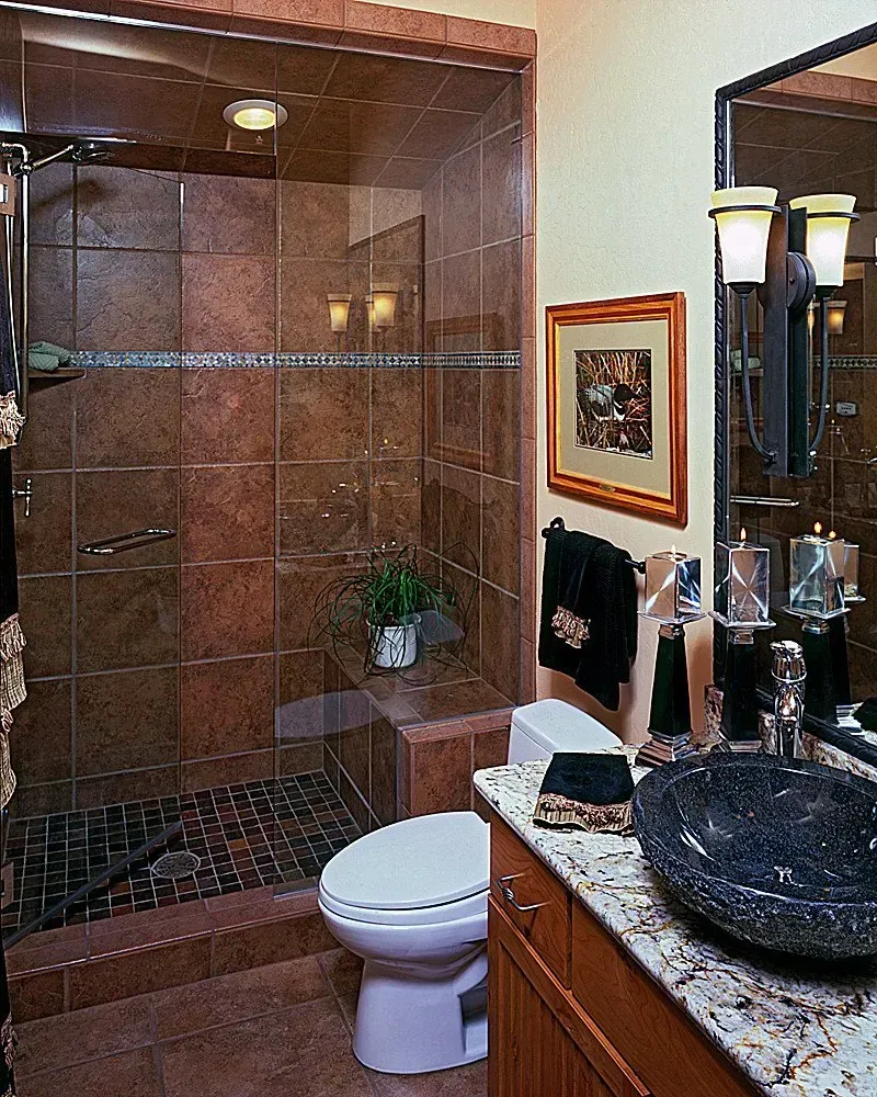 Bathroom with walk-in shower, brown tile, granite countertop with black vessel sink, toilet, framed art, and mirror.