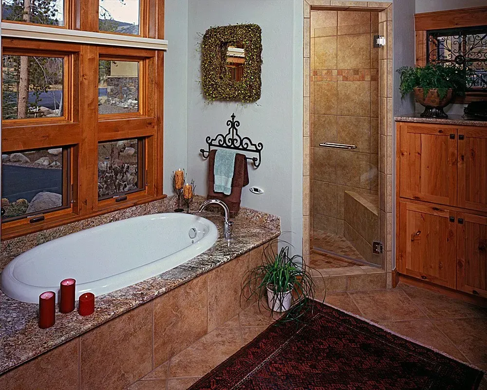 Bathroom with oval tub, granite counter, tile shower, wooden cabinets, and large window.