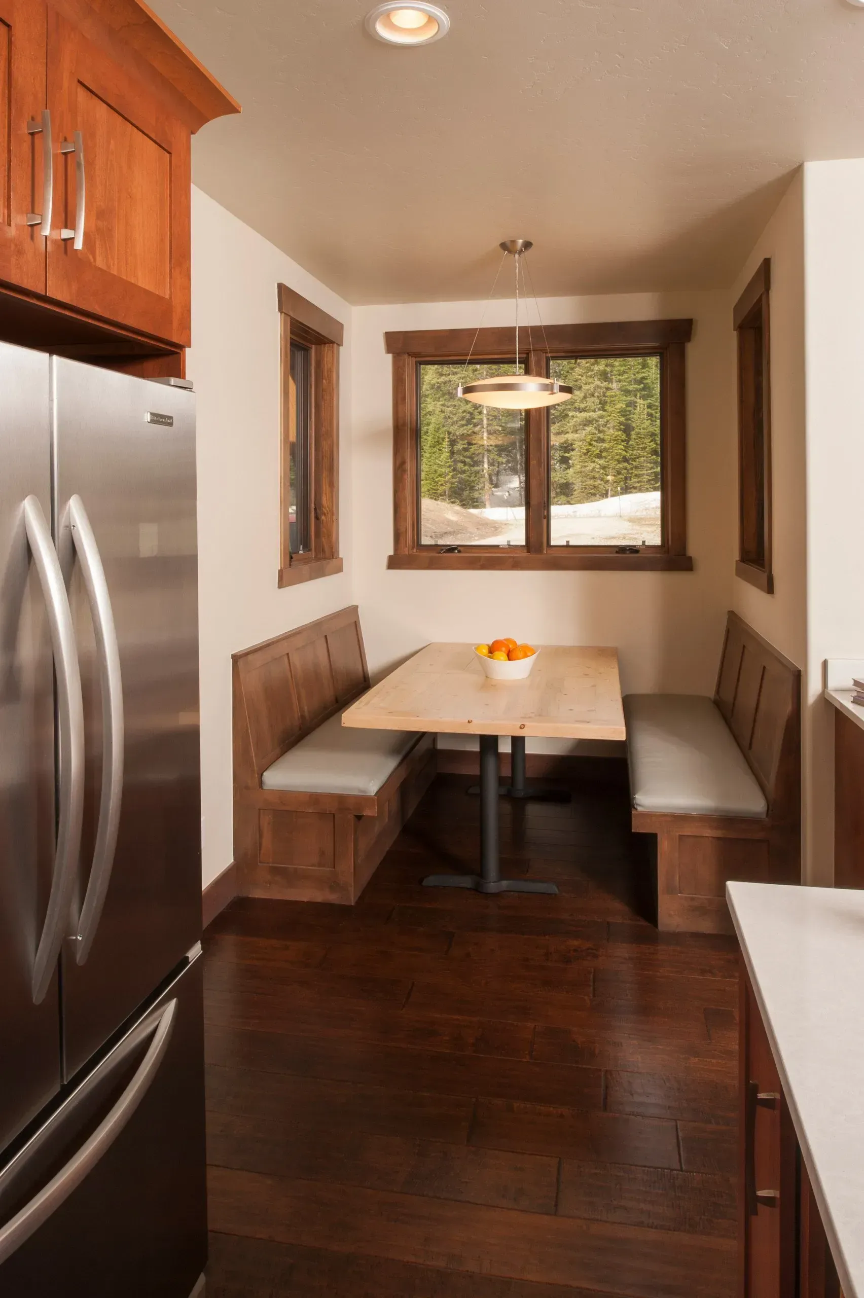 Kitchen nook with wooden benches, table, and a window overlooking a snowy landscape.