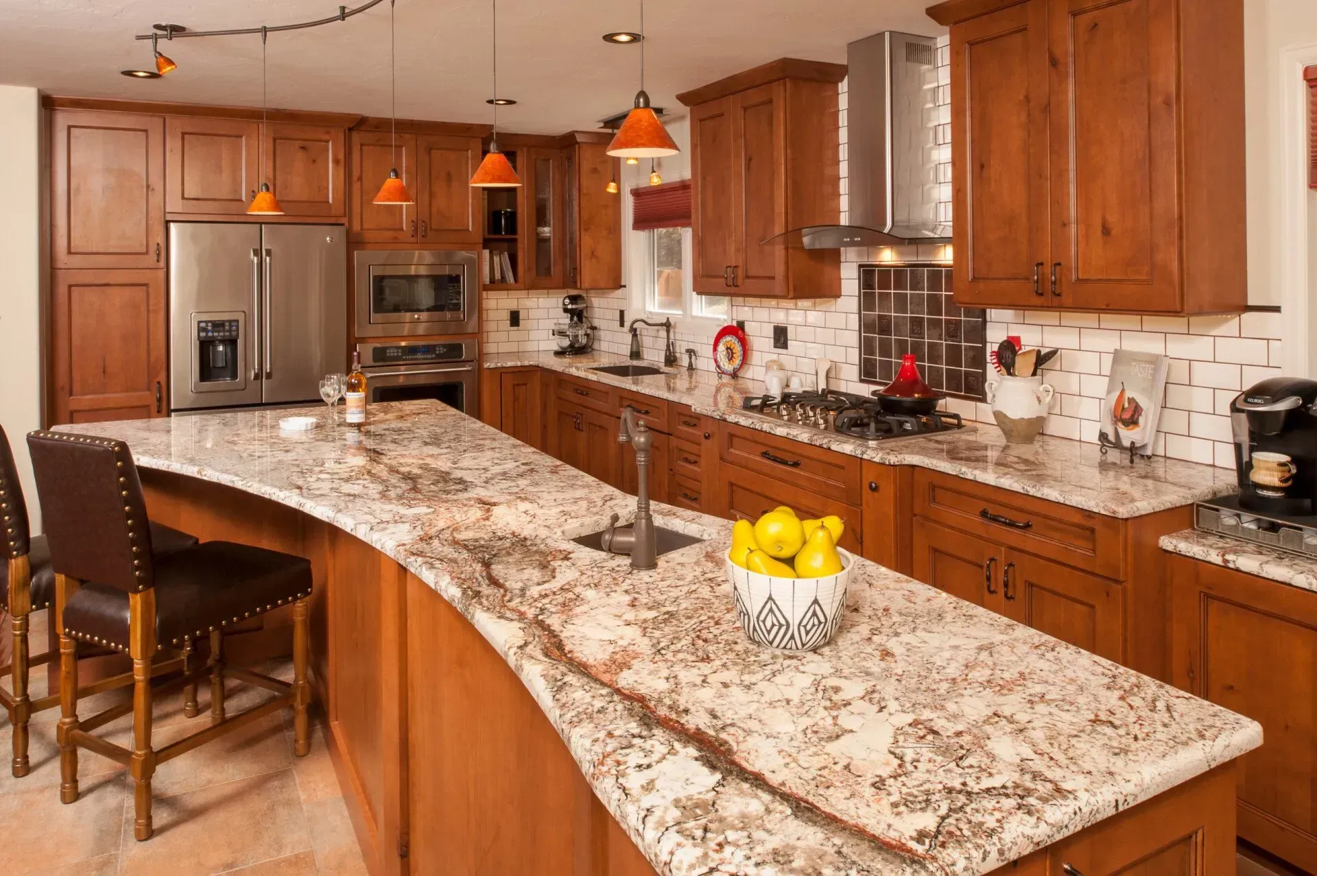Kitchen with wood cabinets, granite countertops, stainless steel appliances, and orange pendant lights.