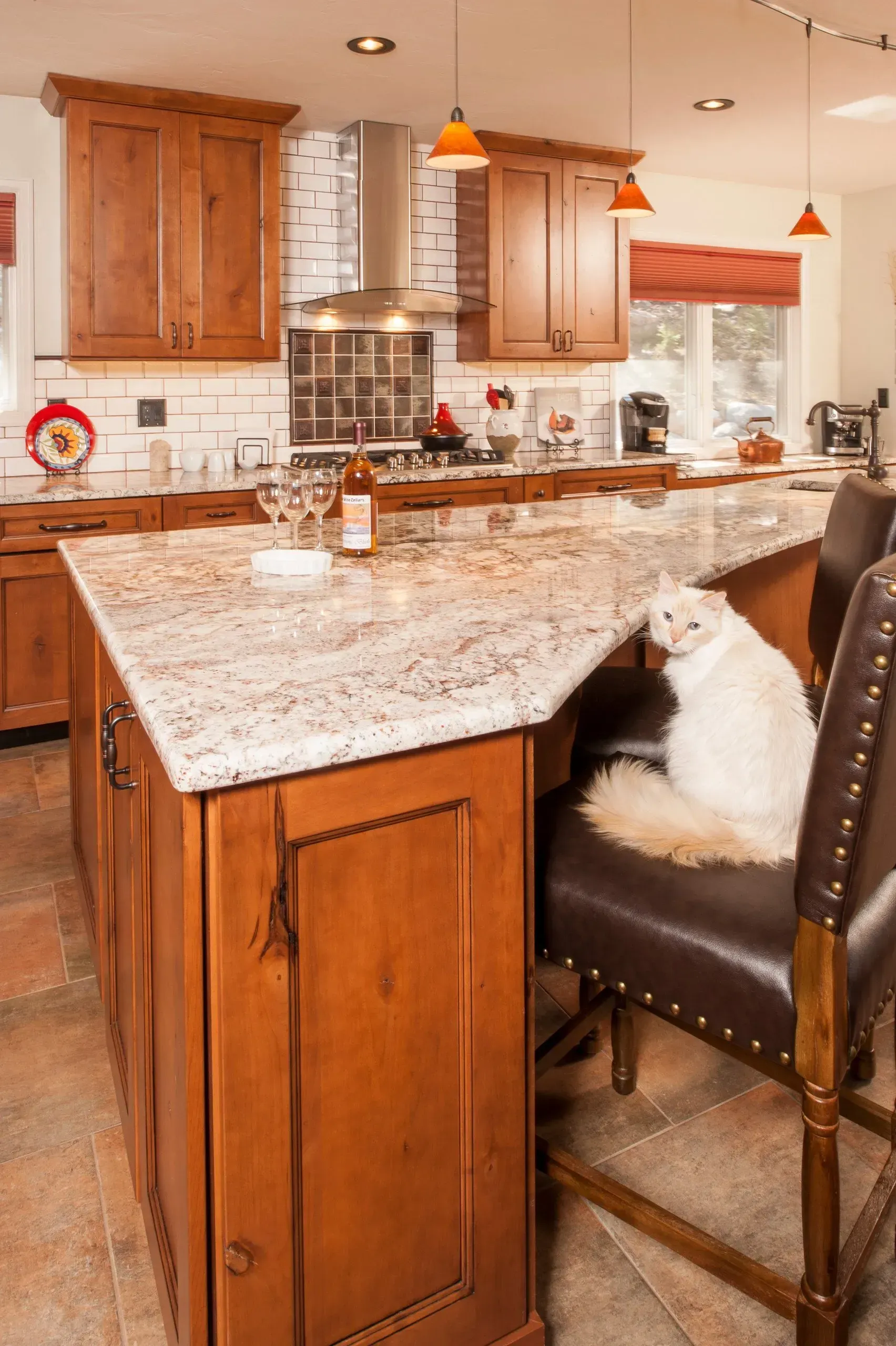 A white cat sits on a leather barstool in a kitchen with a wooden island and granite countertop.