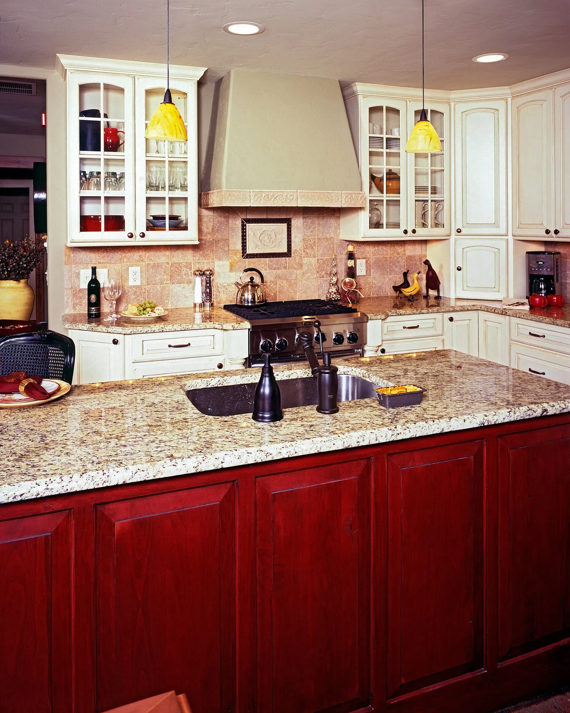 Kitchen with red island, white cabinets, granite countertops, and a stove beneath a muted green vent hood.