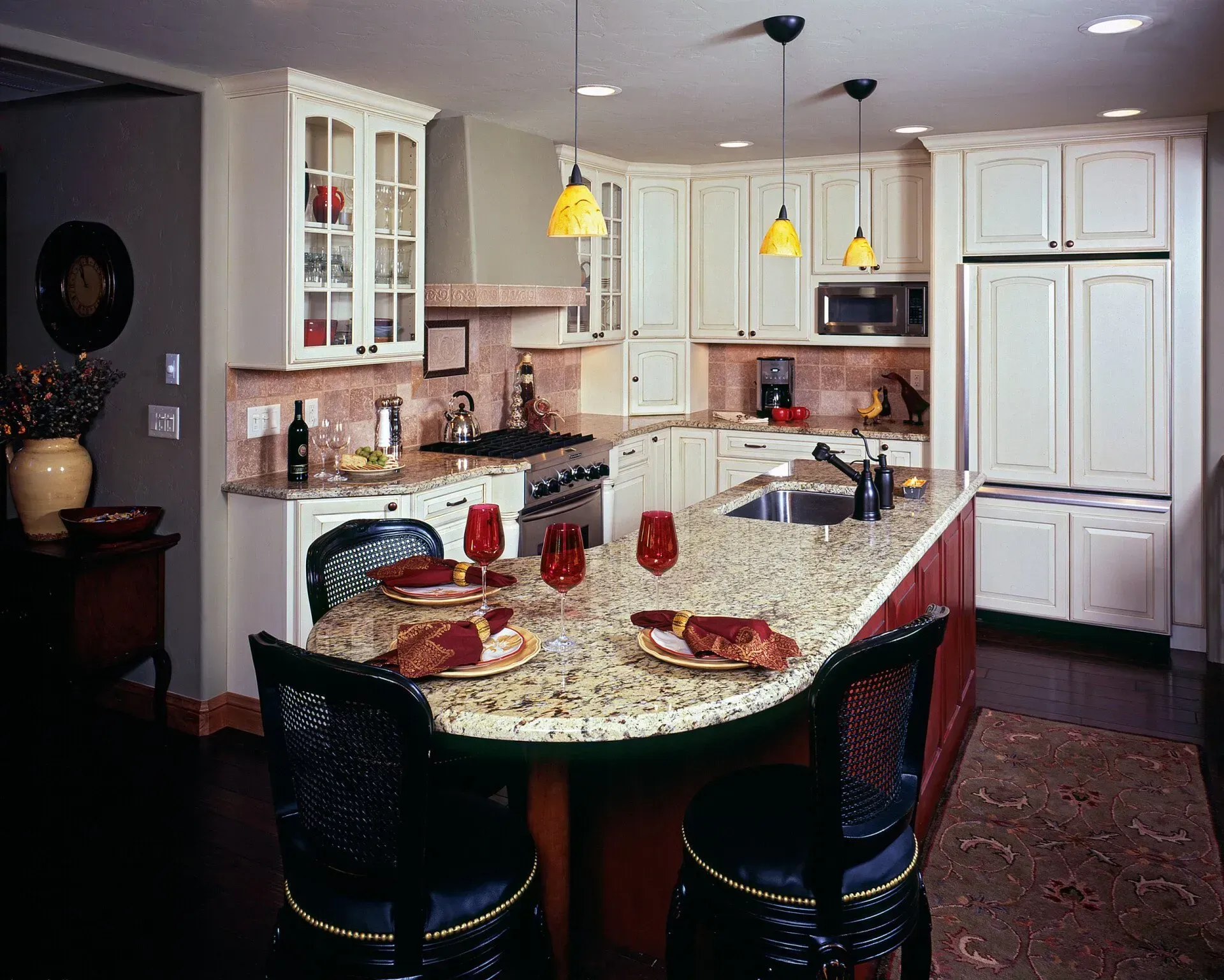 Kitchen with white cabinets, curved granite countertop island with seating, pendant lights.