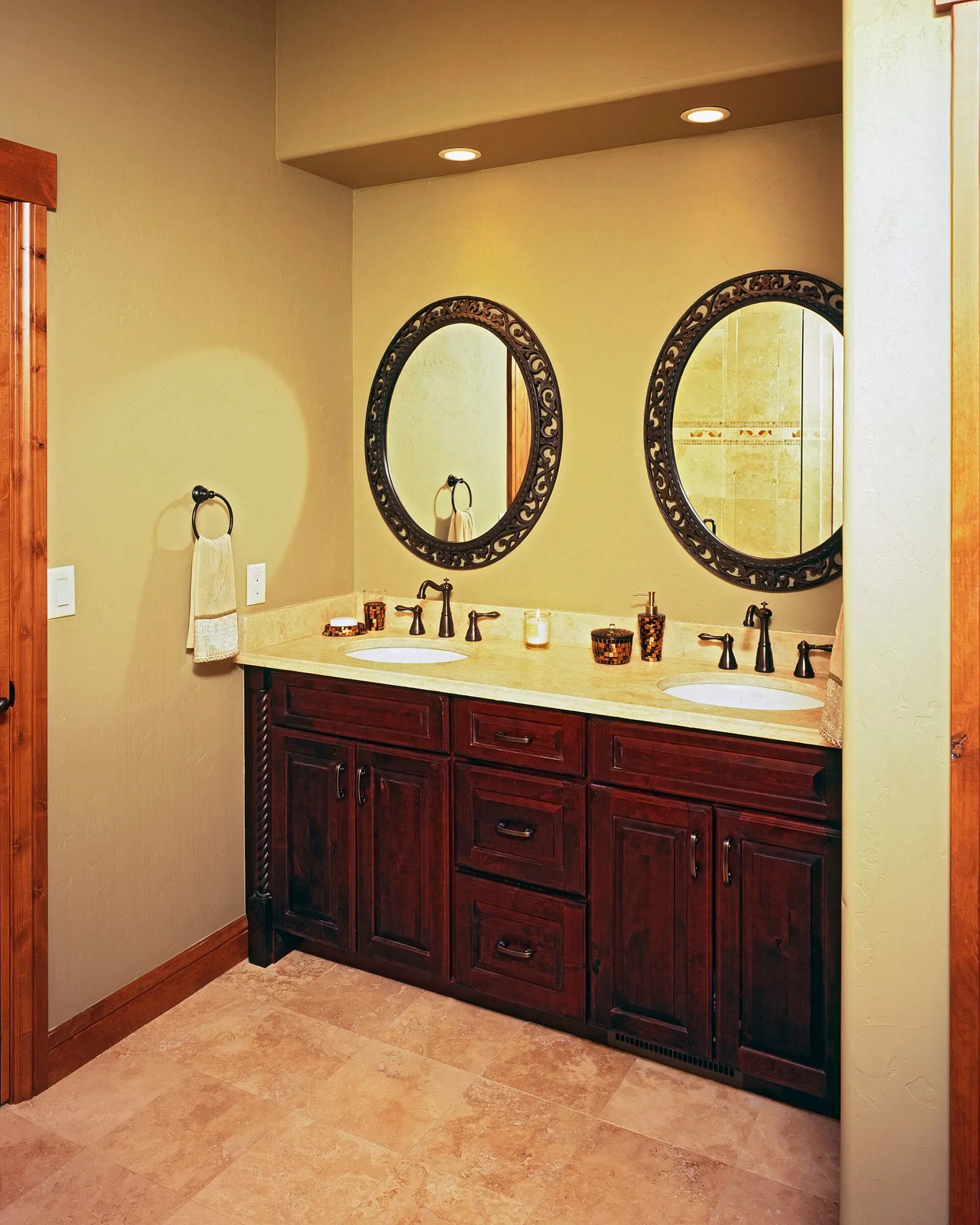 Bathroom with dark wood vanity, oval mirrors, and light-colored tile.