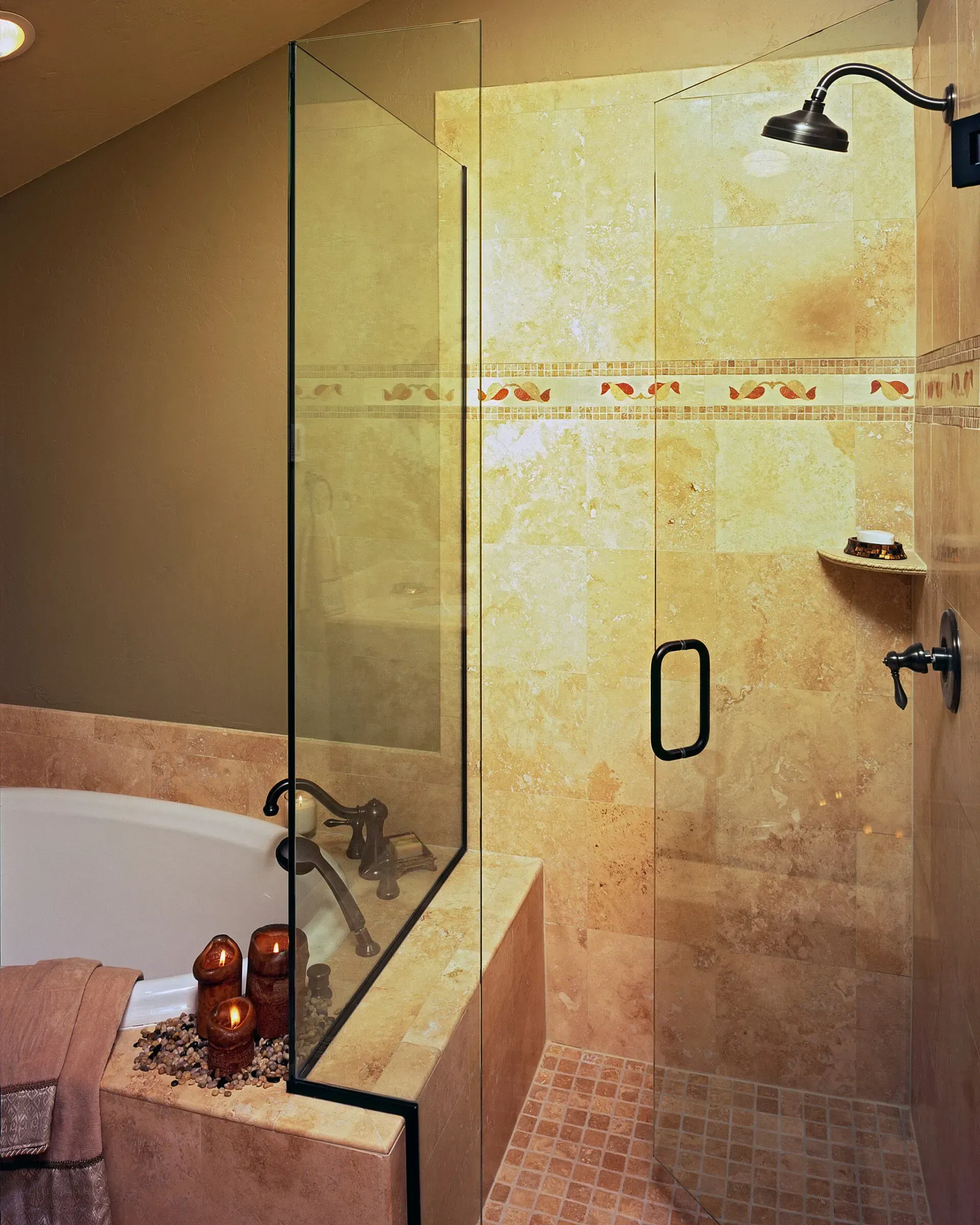Bathroom with a glass shower and stone tile. Features a bathtub and bronze fixtures.