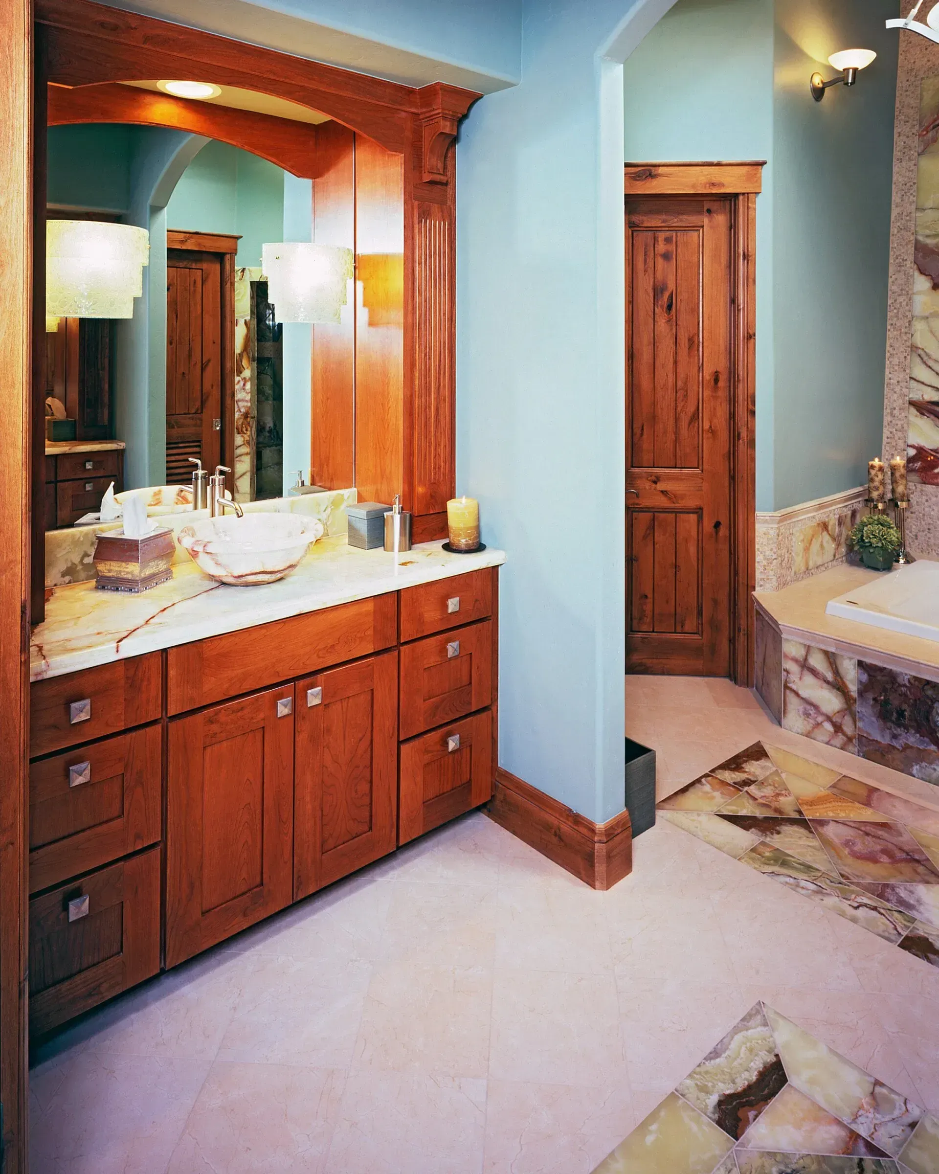 Bathroom with wooden vanity, mirror, and door, pale blue walls, and stone floor.
