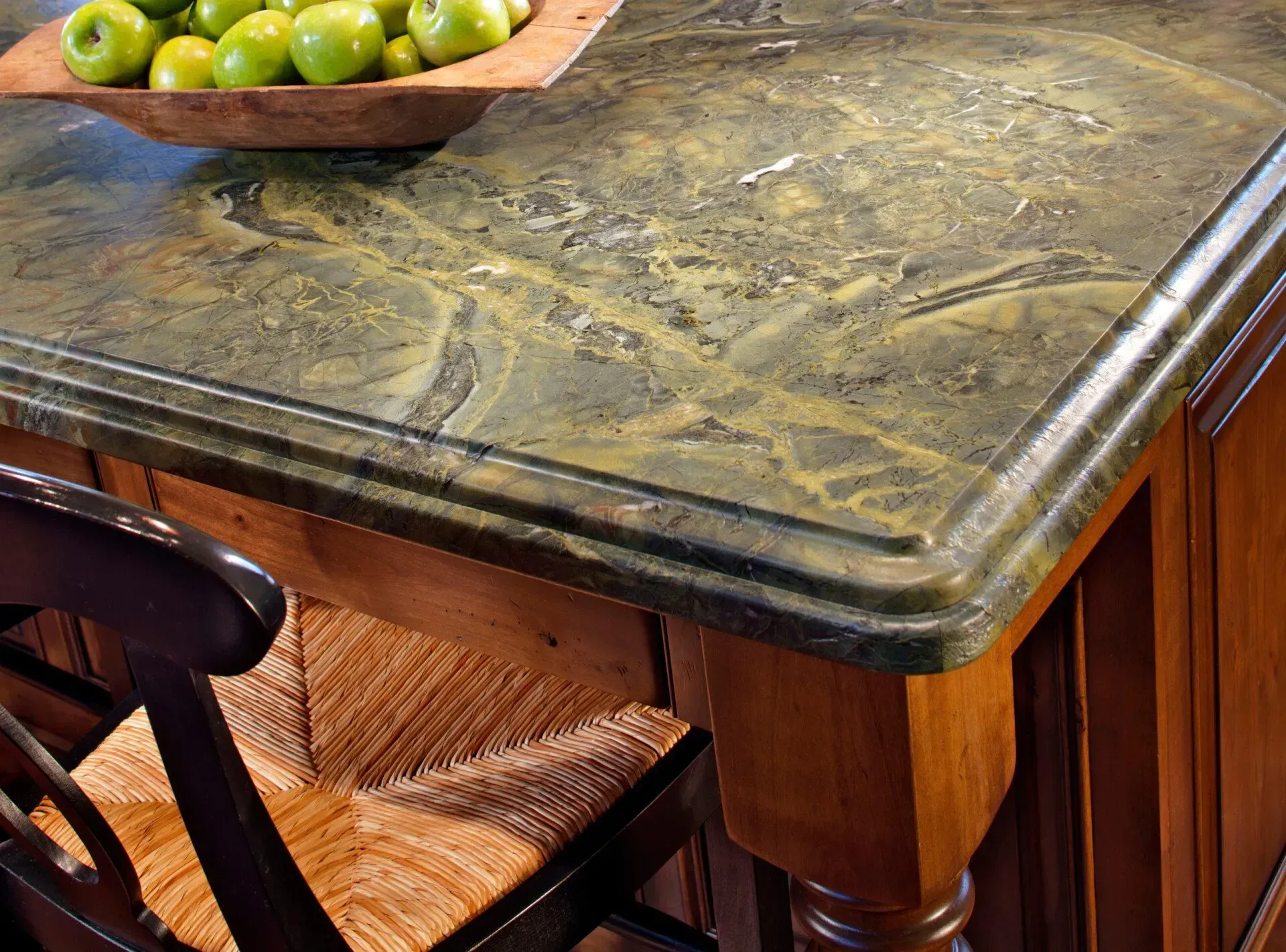 Green and gold mottled countertop with a wooden edge detail, next to a wooden cabinet and chair.