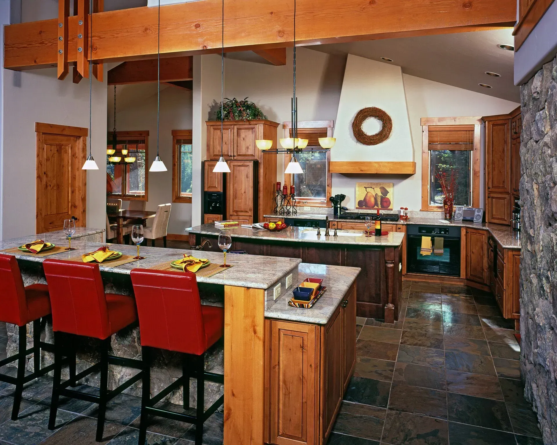 Spacious kitchen with wood cabinets, granite countertops, stone floor, and red bar stools.