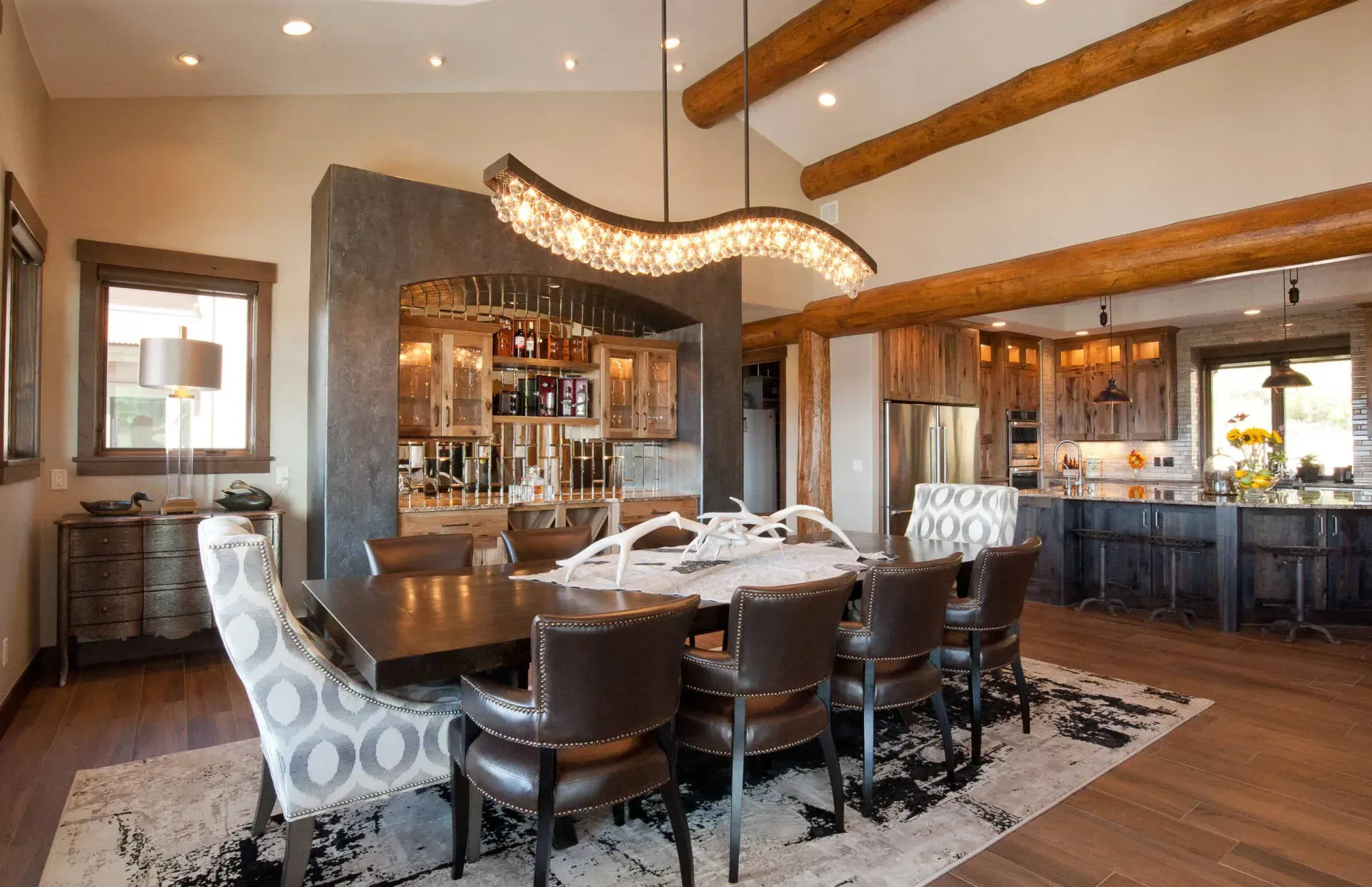 Spacious dining room with dark wood table, leather chairs, and crystal chandelier, open to kitchen and bar area.
