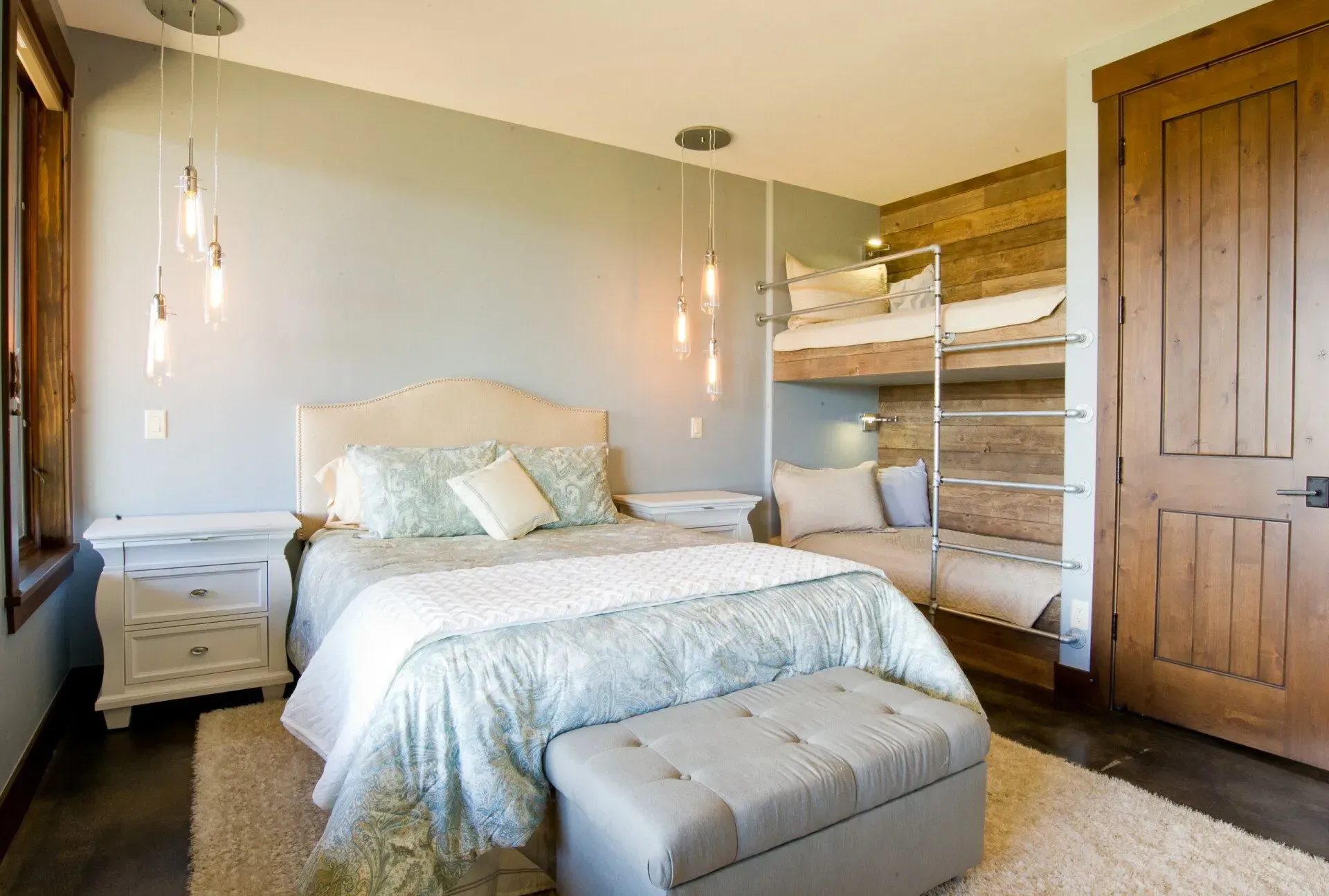 Bedroom with a bed, bunk beds, and a bench. Light blue walls, wood door, and pendant lights.