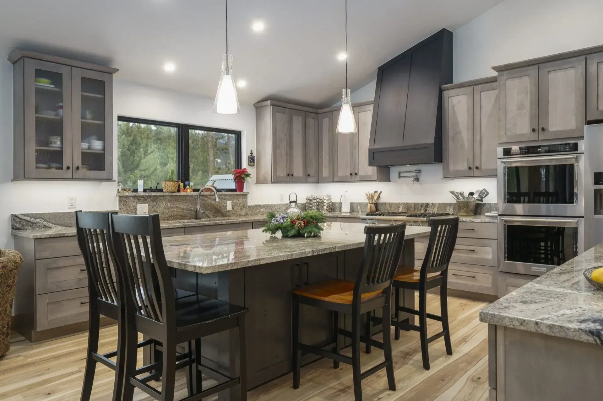 Spacious kitchen with gray cabinets, granite countertops, an island with bar stools, and a black range hood.