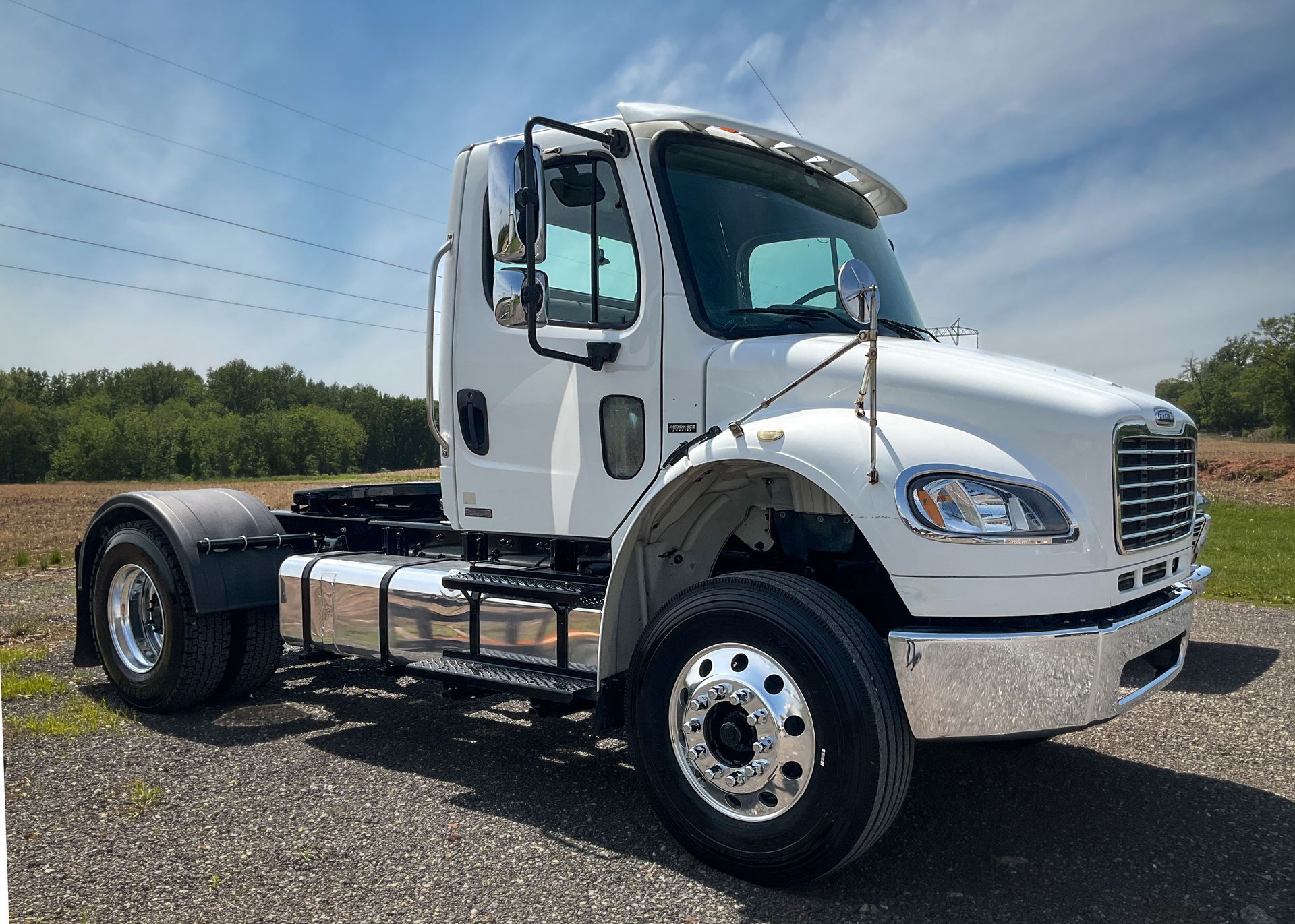 White Freightliner truck parked on gravel, sunny day.