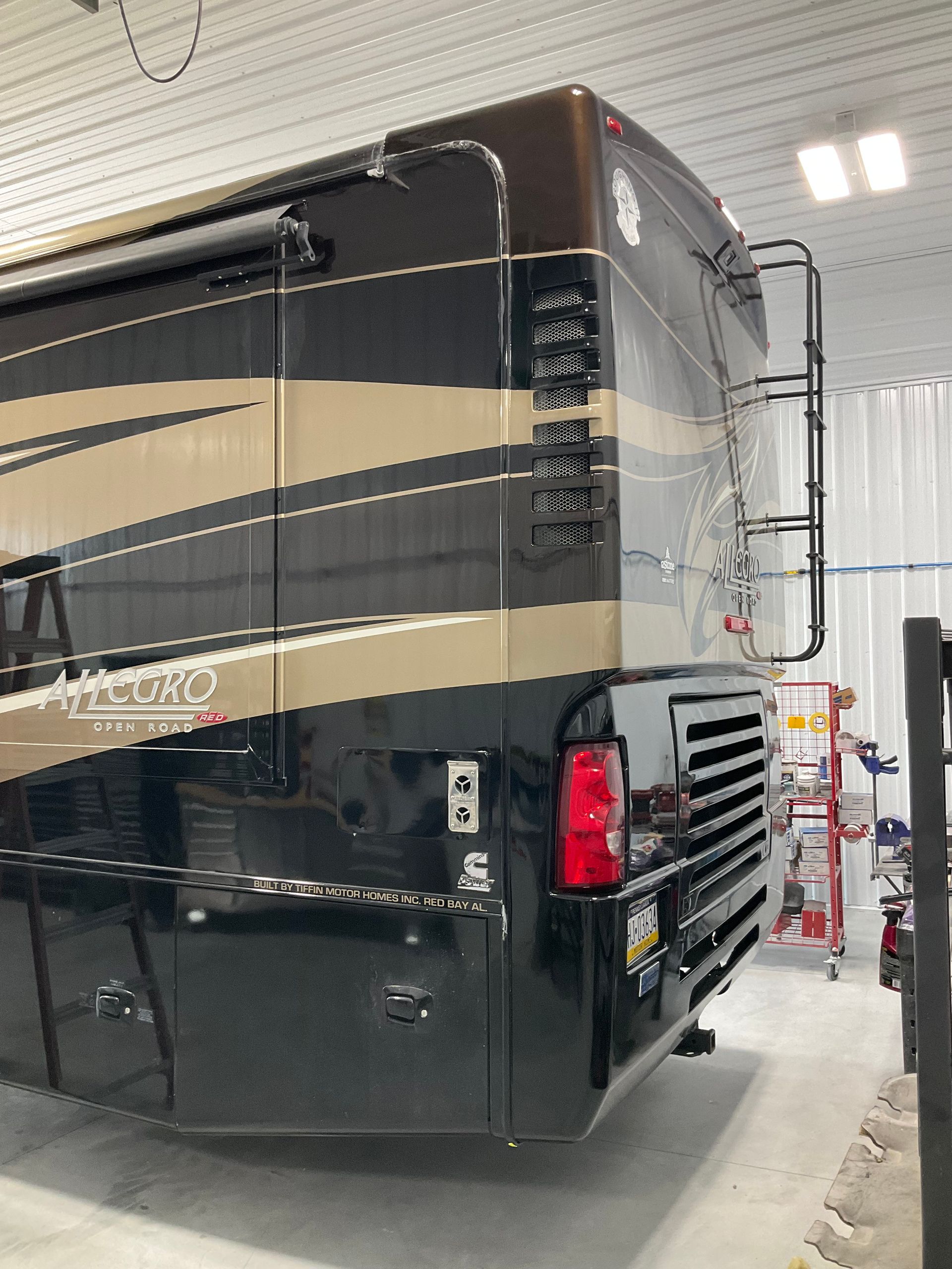 Black and gold RV rear view with ladder and taillight in a garage.