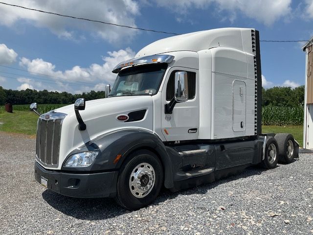 White Peterbilt semi-truck parked outdoors on a gravel lot under a blue sky with white clouds.